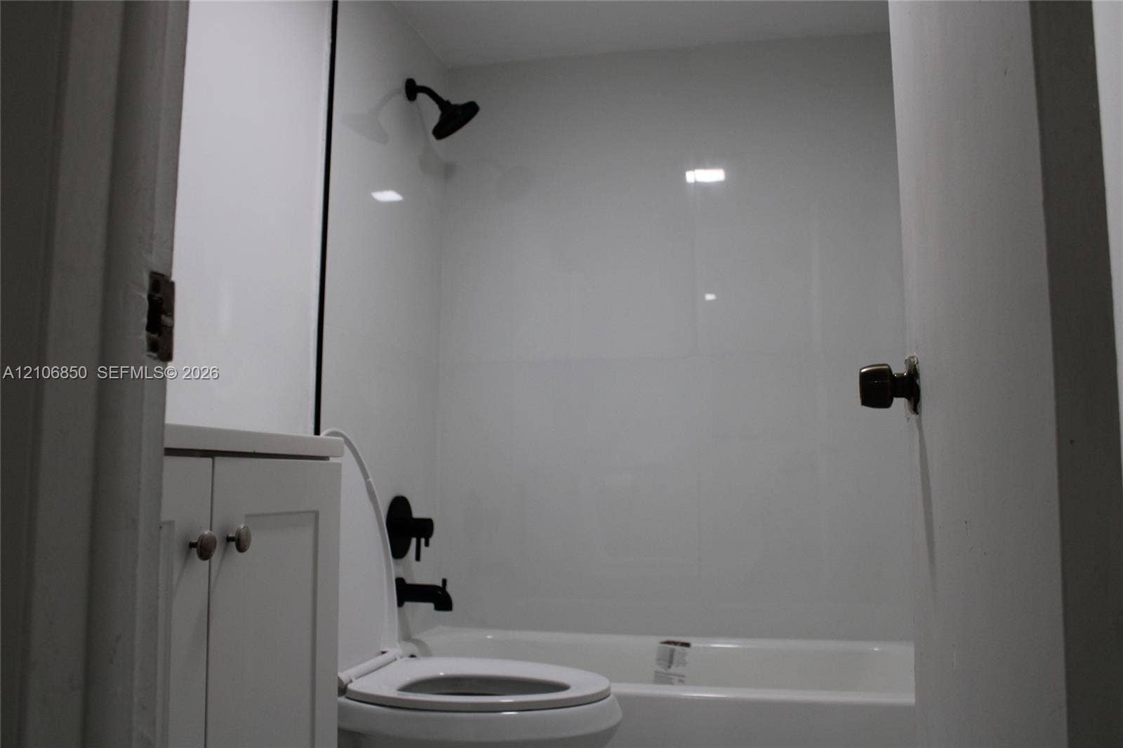 Bathroom featuring white panel shower surround, matte black showerhead and tub faucet, white vanity cabinet with circular pulls, and white standard toilet