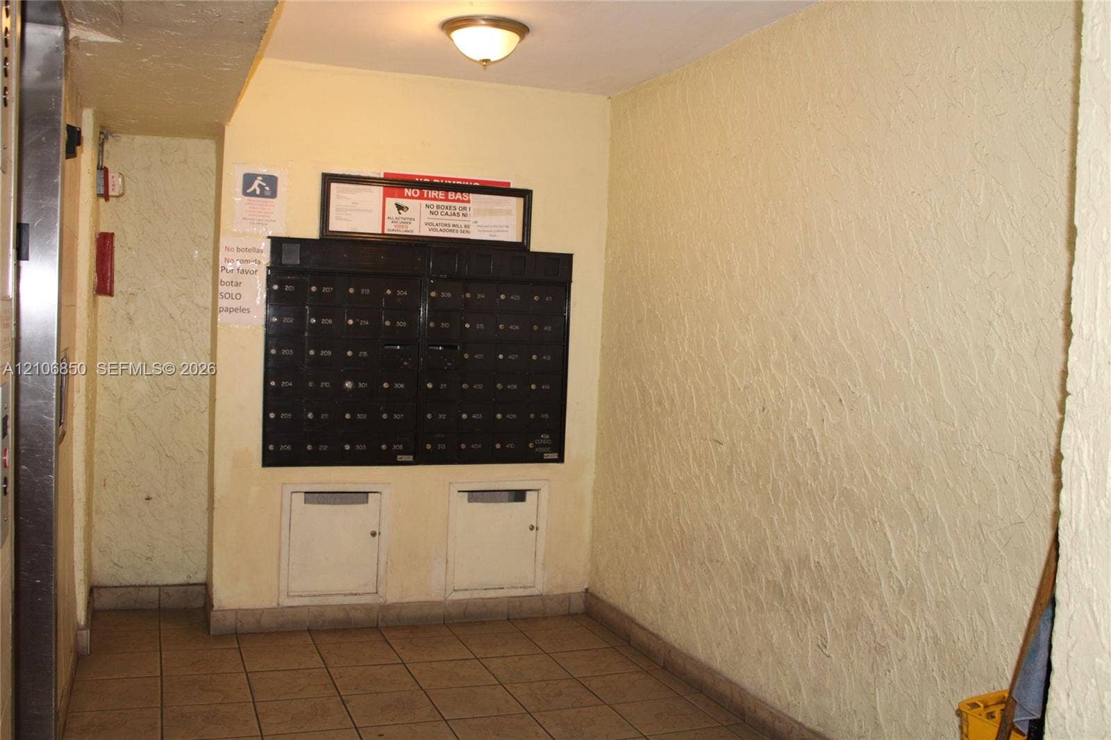 Common area mail center featuring a multi-unit black metal mailbox station, tiled flooring, and a ceiling-mounted light fixture