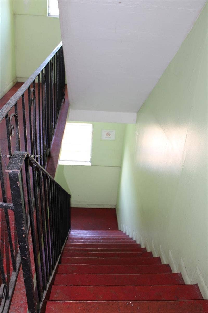Stairwell featuring painted red treads and a metal railing with decorative scrollwork