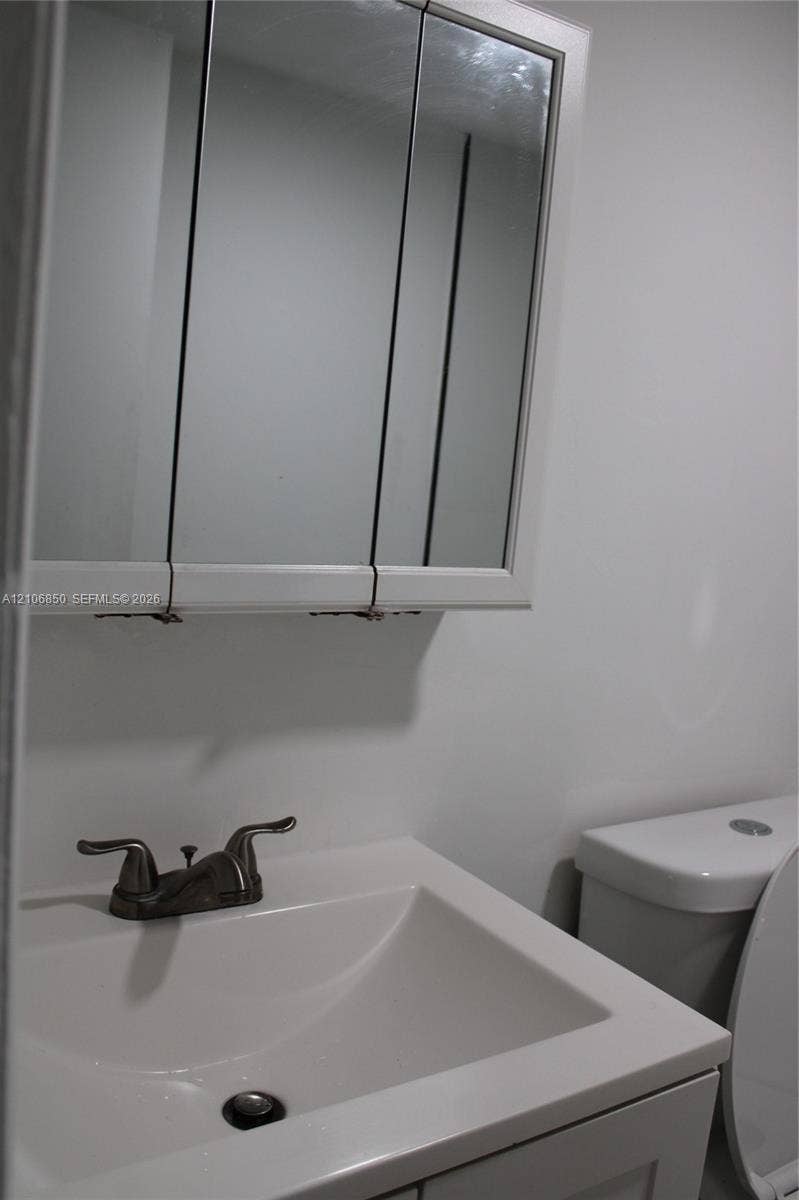 Tri-fold mirrored medicine cabinet, solid-surface vanity countertop with integrated basin, and dual-handle metallic faucet
