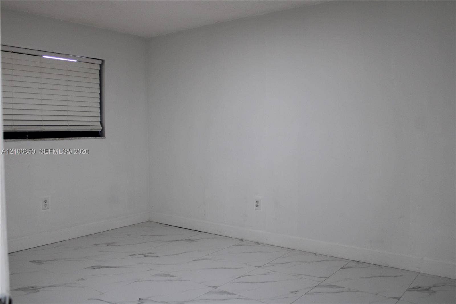 Neutral-toned interior space featuring light-colored tile flooring with a marble-finish pattern and a window equipped with horizontal blinds
