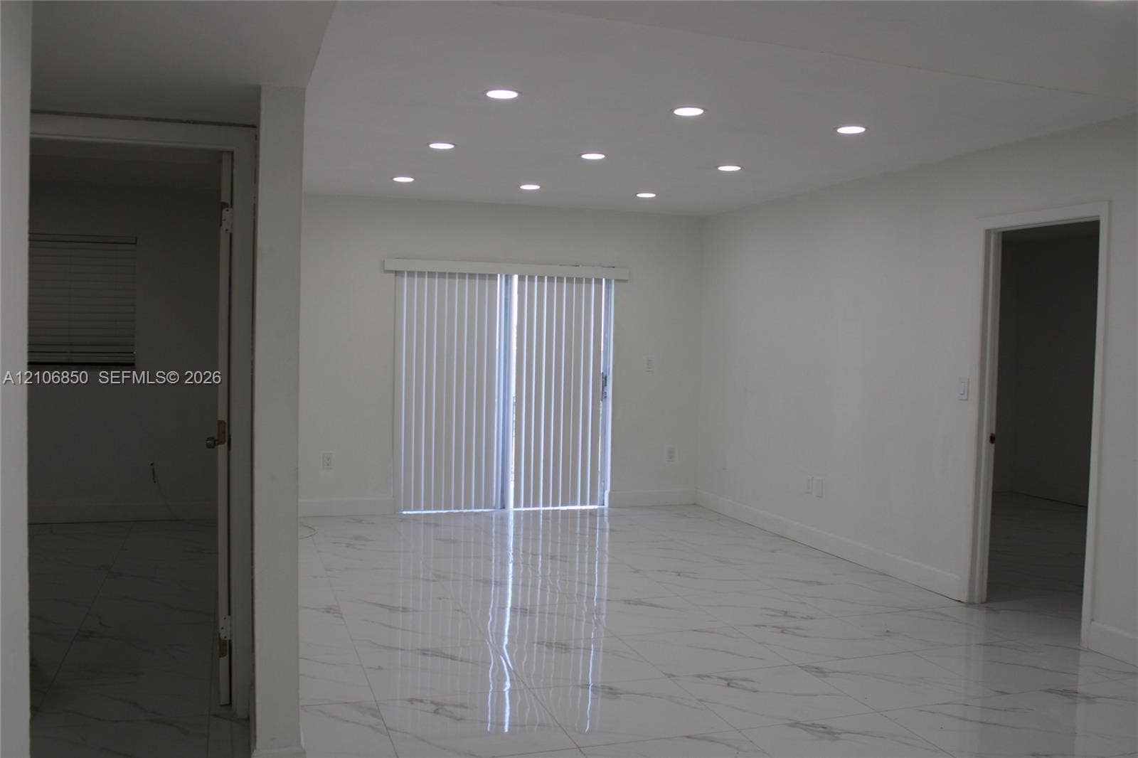 Interior space featuring large-format stone-finish tile flooring, recessed ceiling lighting, and sliding glass doors with vertical blinds