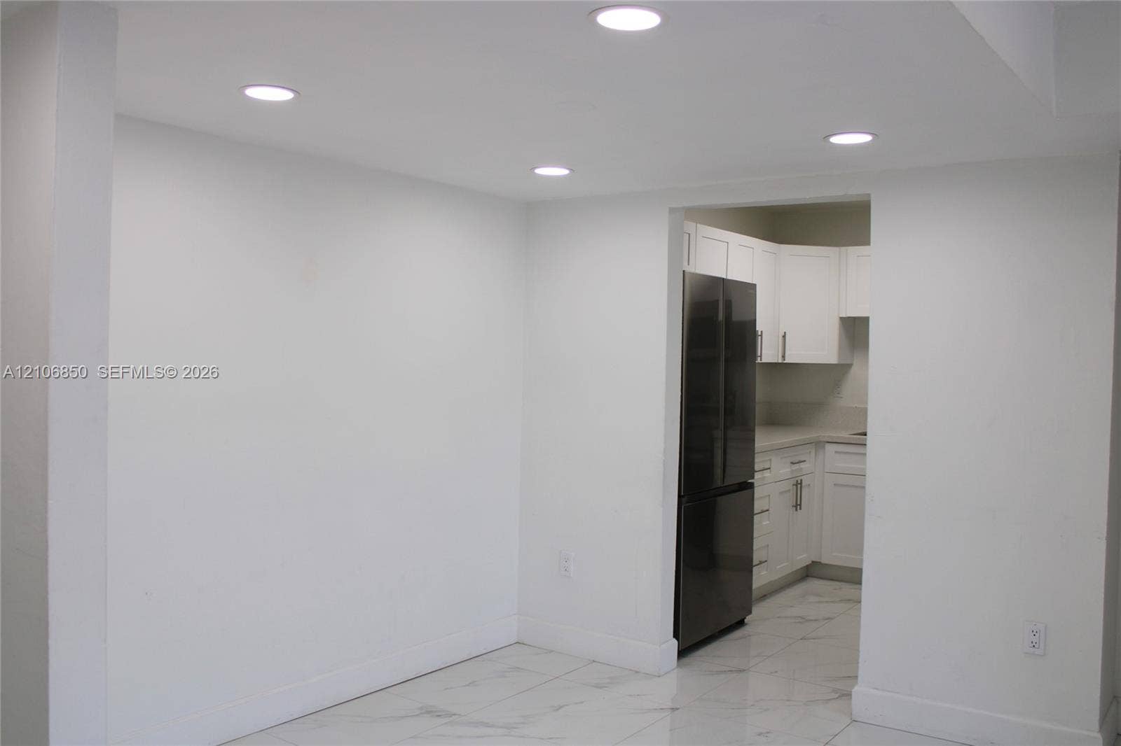 Recessed ceiling lighting, large-format tile flooring, and white Shaker-style cabinetry with neutral countertops and a stainless steel refrigerator