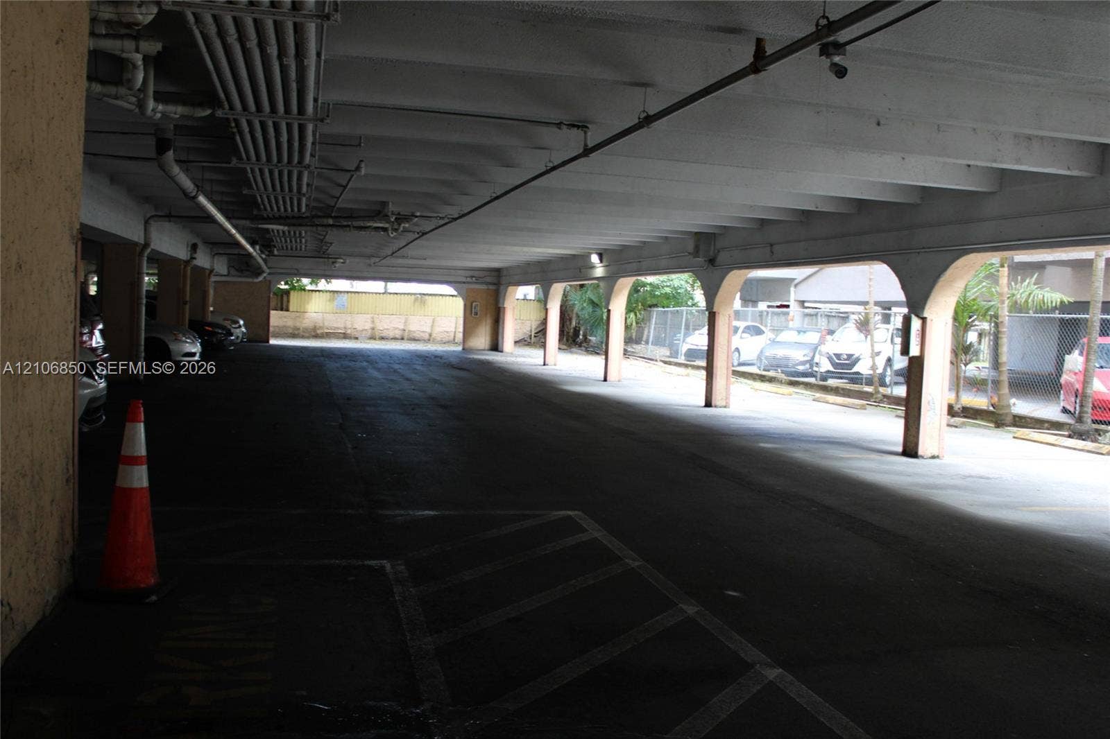 Covered parking area featuring concrete pillars, arched openings, and a paved surface