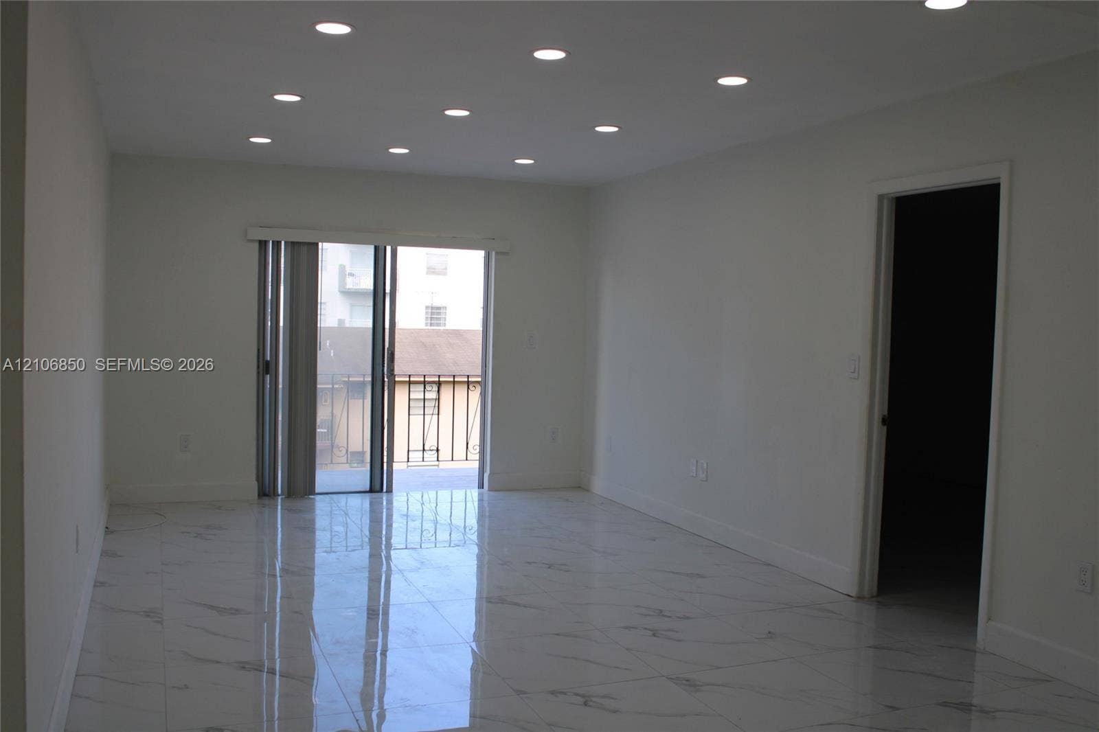 Interior space featuring high-gloss tile flooring with veining detail, recessed ceiling lighting, and sliding glass door access to an exterior balcony