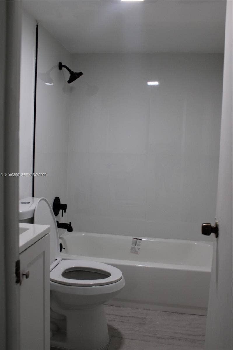 Full bathroom featuring a tub-shower combination with matte black fixtures, white surround, and a vanity cabinet