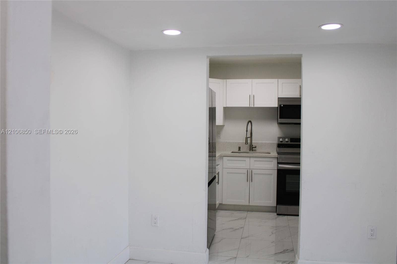 Kitchen featuring white shaker-style cabinetry, stainless steel appliances, a pull-down kitchen faucet, and stone-finish floor tiling with integrated recessed lighting