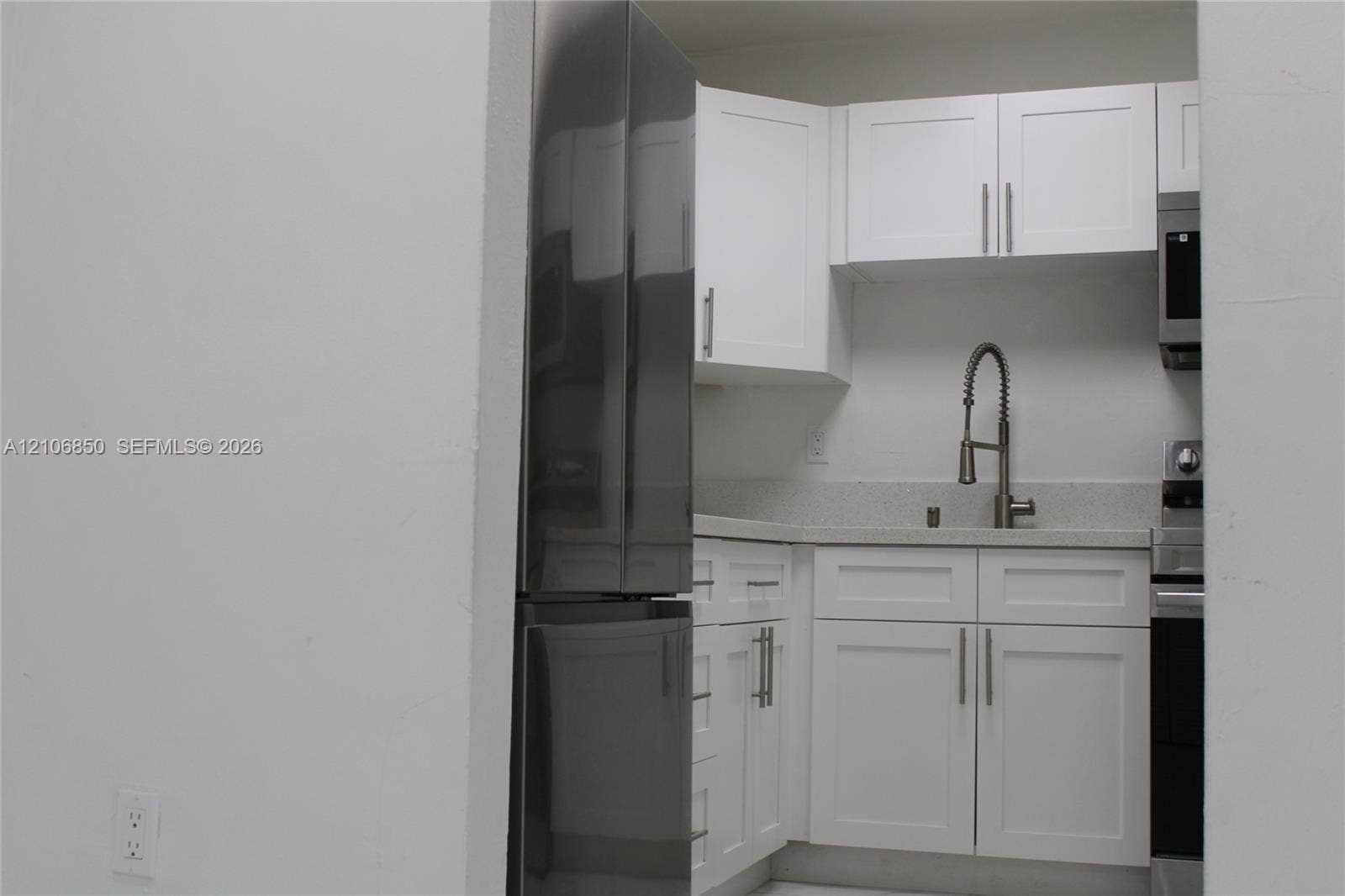 Kitchen featuring white shaker-style cabinetry, stainless steel refrigerator, stone-composite countertop, undermount sink with gooseneck faucet, and stainless steel microwave