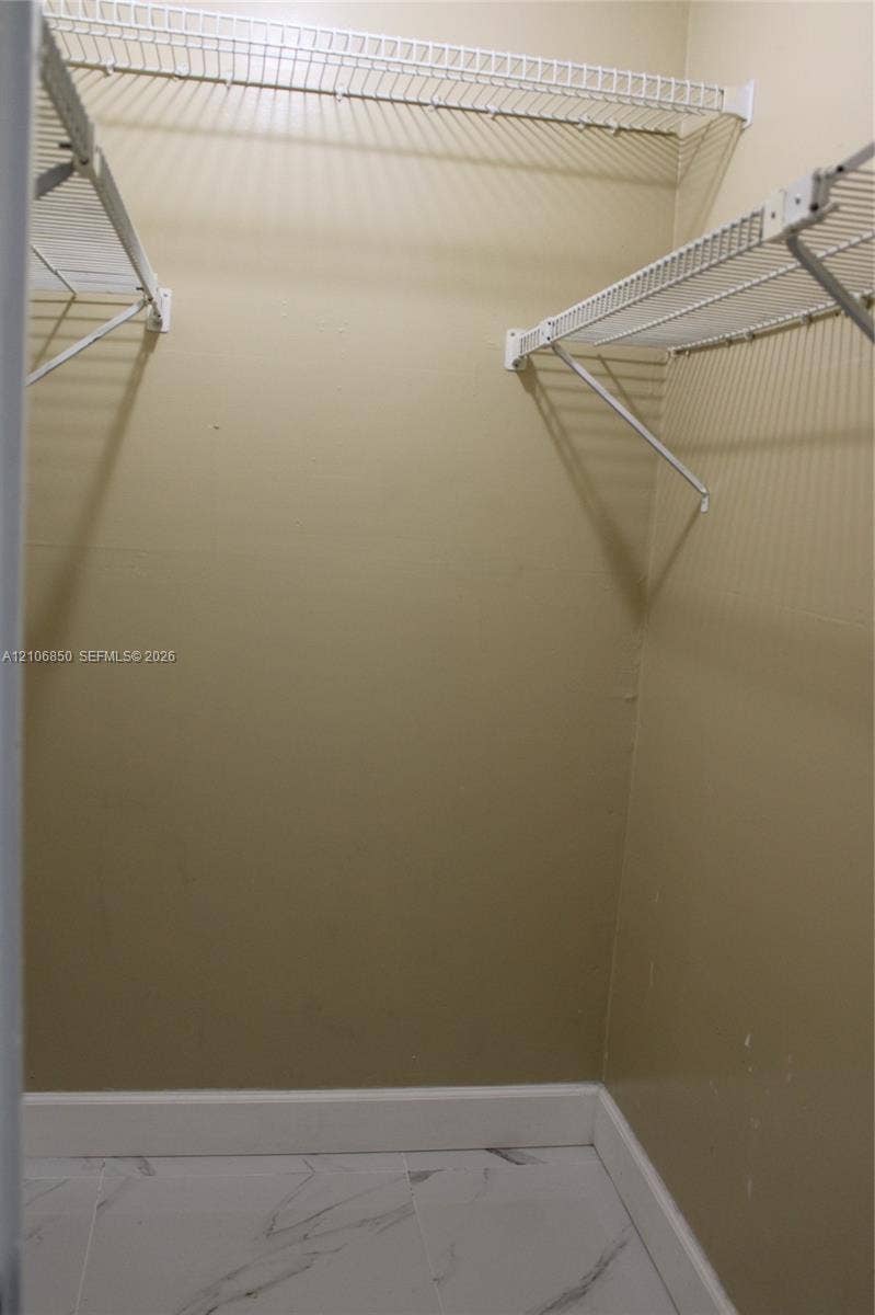 Walk-in closet featuring white wire shelving and large-format tile flooring with a marble-finish pattern