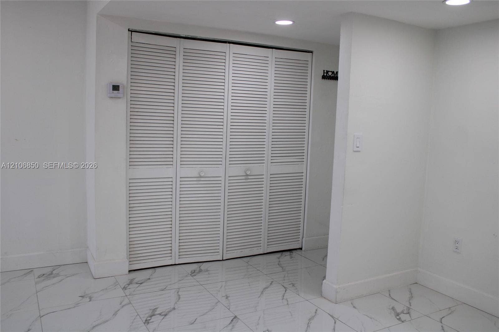 White louvered folding closet doors featuring circular hardware, complemented by large-format white tile flooring with grey veining and recessed ceiling lighting