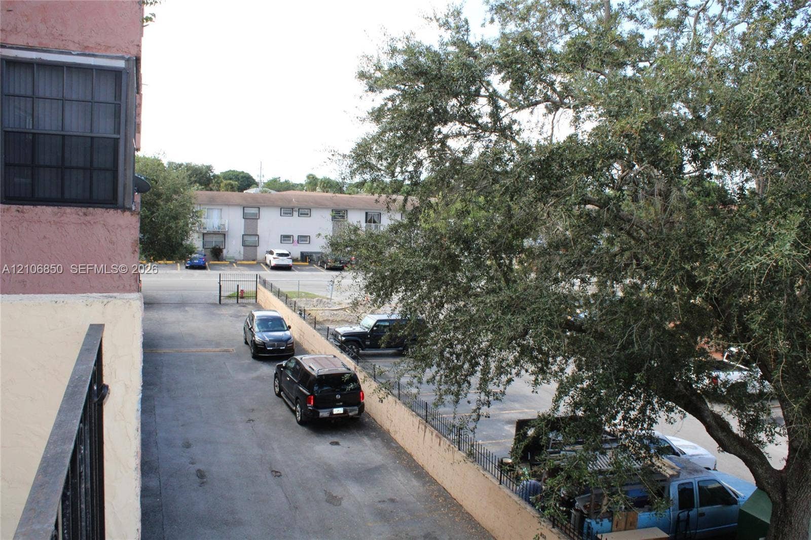 Exterior view featuring metal balcony railing, paved surface parking lot, and mature trees