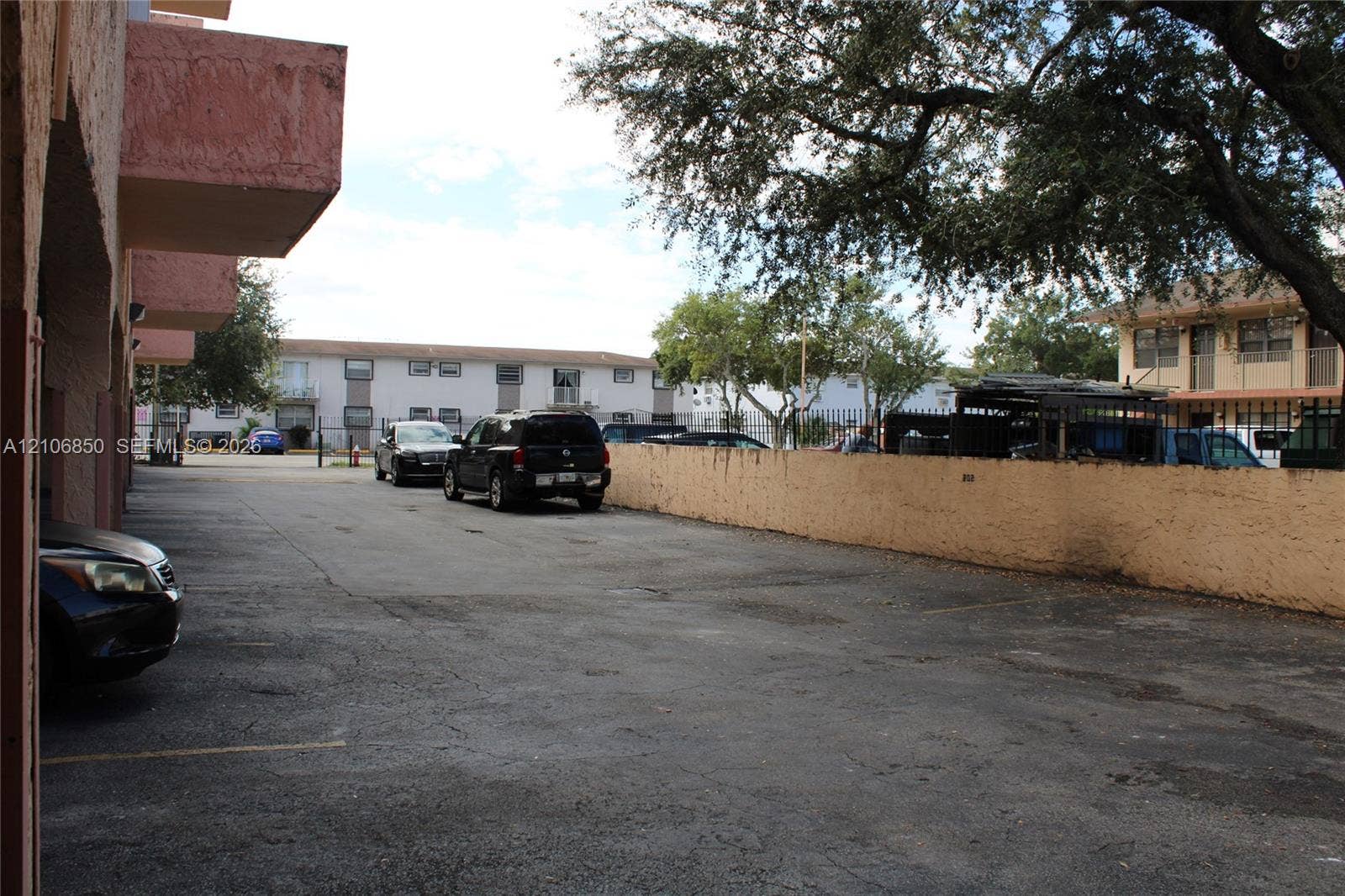 Asphalt-paved off-street parking area enclosed by a masonry perimeter wall and mature tree canopy