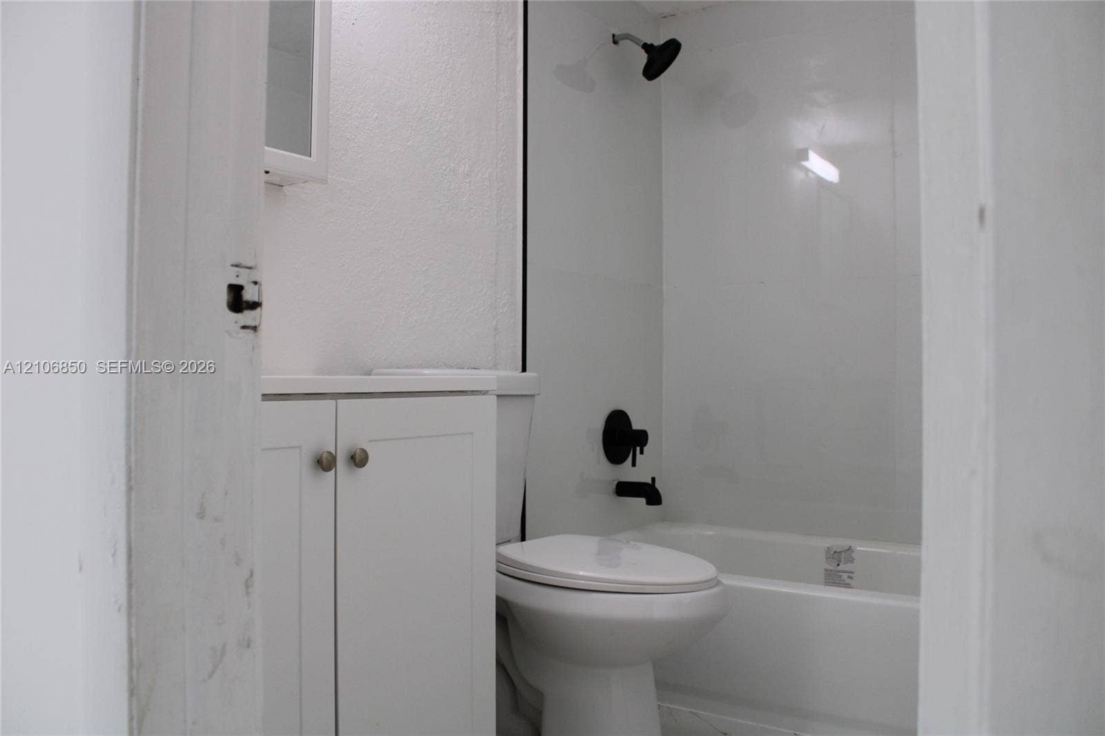 Bathroom featuring white shaker-style cabinetry, matte black hardware, wall-mounted shower head, and a white bathtub surround
