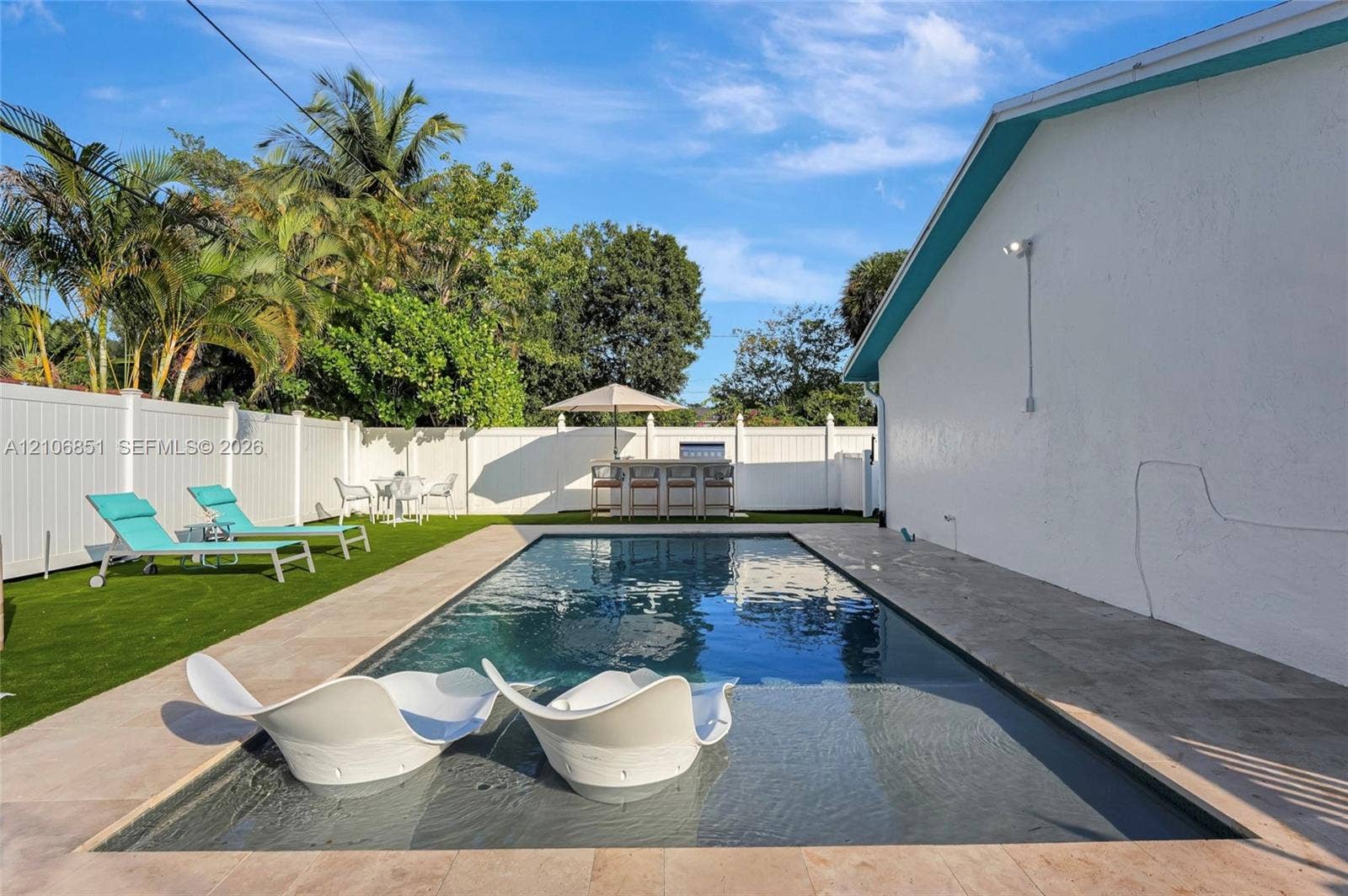1319 SW 30th Street, #B, Fort Lauderdale, Fort Lauderdale, FL 33315 In-ground swimming pool with shallow tanning ledge, complemented by light-toned stone paver decking and synthetic turf lawn, all enclosed by white vinyl privacy fencing