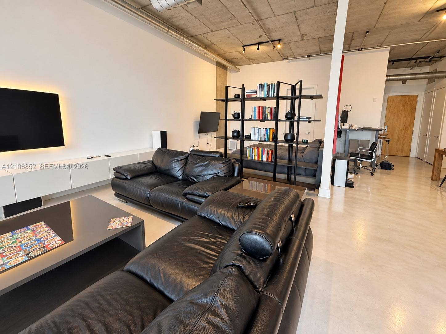 Industrial-style living space featuring an exposed concrete ceiling, polished concrete flooring, built-in wall-mounted cabinetry, and exposed ductwork