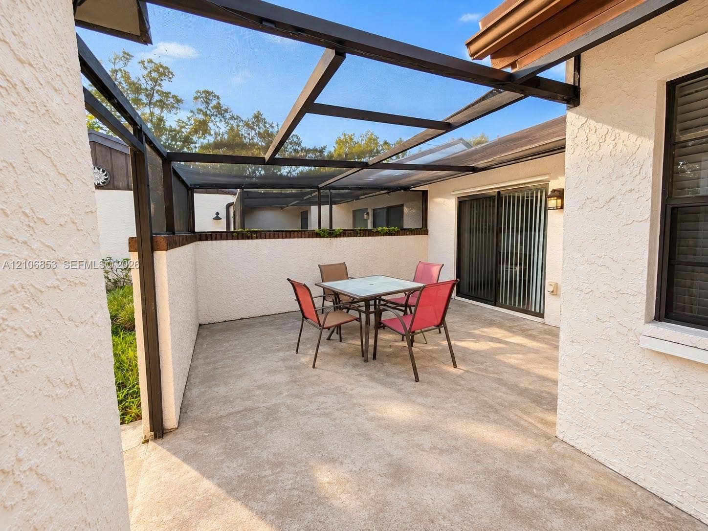 6331 Pinehurst Circle W, #C35, Tamarac, FL 33321 Enclosed concrete patio featuring a black-framed screen roof, stucco walls, and sliding glass door access