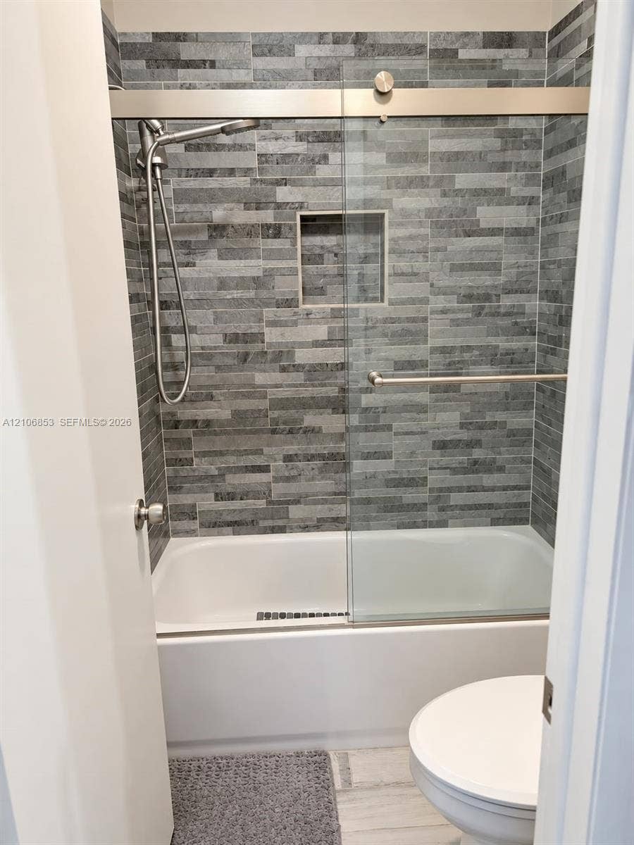 6331 Pinehurst Circle W, #C35, Tamarac, FL 33321 Walk-in shower enclosure featuring stacked stone wall tile, built-in recessed wall niche, sliding glass door, and stainless steel hand-held shower fixture