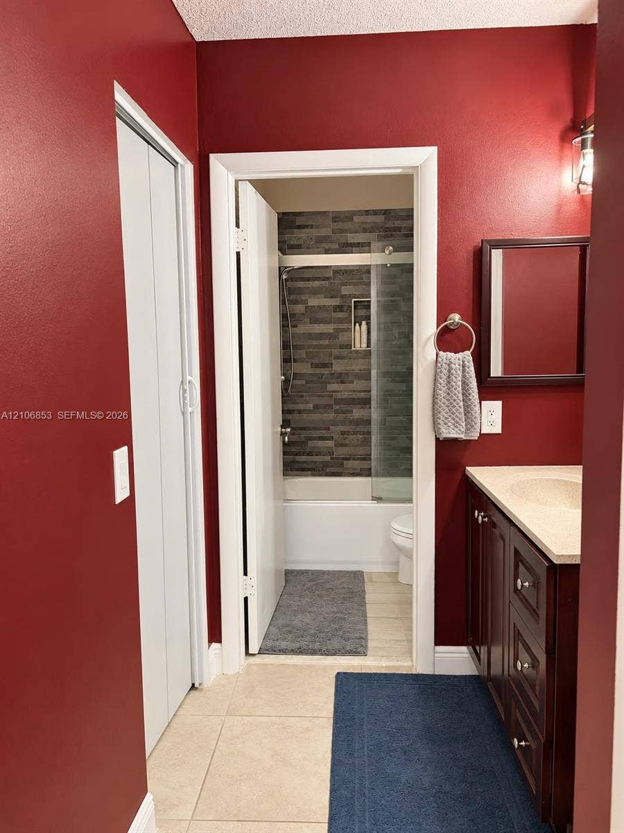 6331 Pinehurst Circle W, #C35, Tamarac, FL 33321 Bathroom featuring dark wood-finish cabinetry, a neutral stone-surface countertop, tiled flooring, and a glass-enclosed shower with horizontal textured wall tile