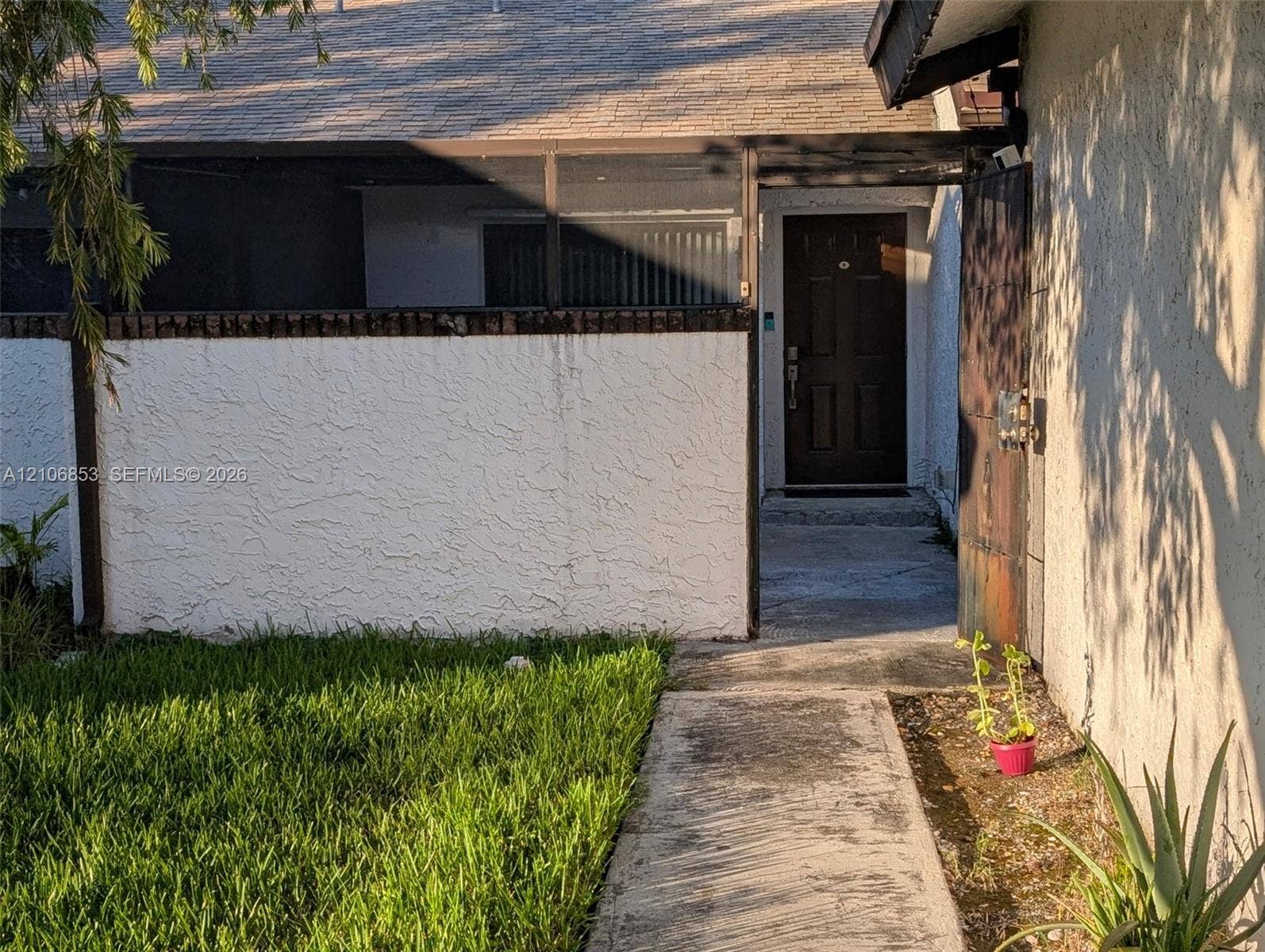 6331 Pinehurst Circle W, #C35, Tamarac, FL 33321 Enclosed entryway featuring a concrete walkway, textured stucco exterior walls, a screened-in porch area, and a solid-panel front door