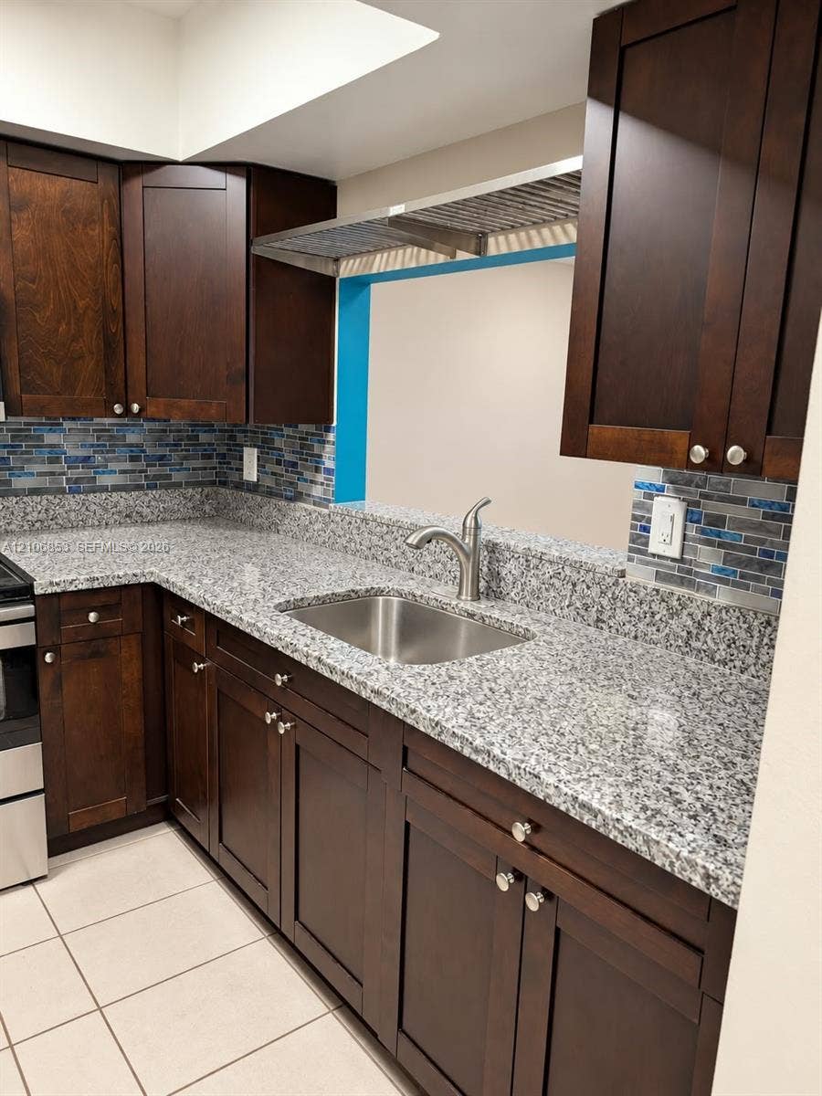 6331 Pinehurst Circle W, #C35, Tamarac, FL 33321 Dark-toned wood cabinetry, stone-surface countertops, stainless steel undermount sink, gooseneck faucet, and mosaic tile backsplash