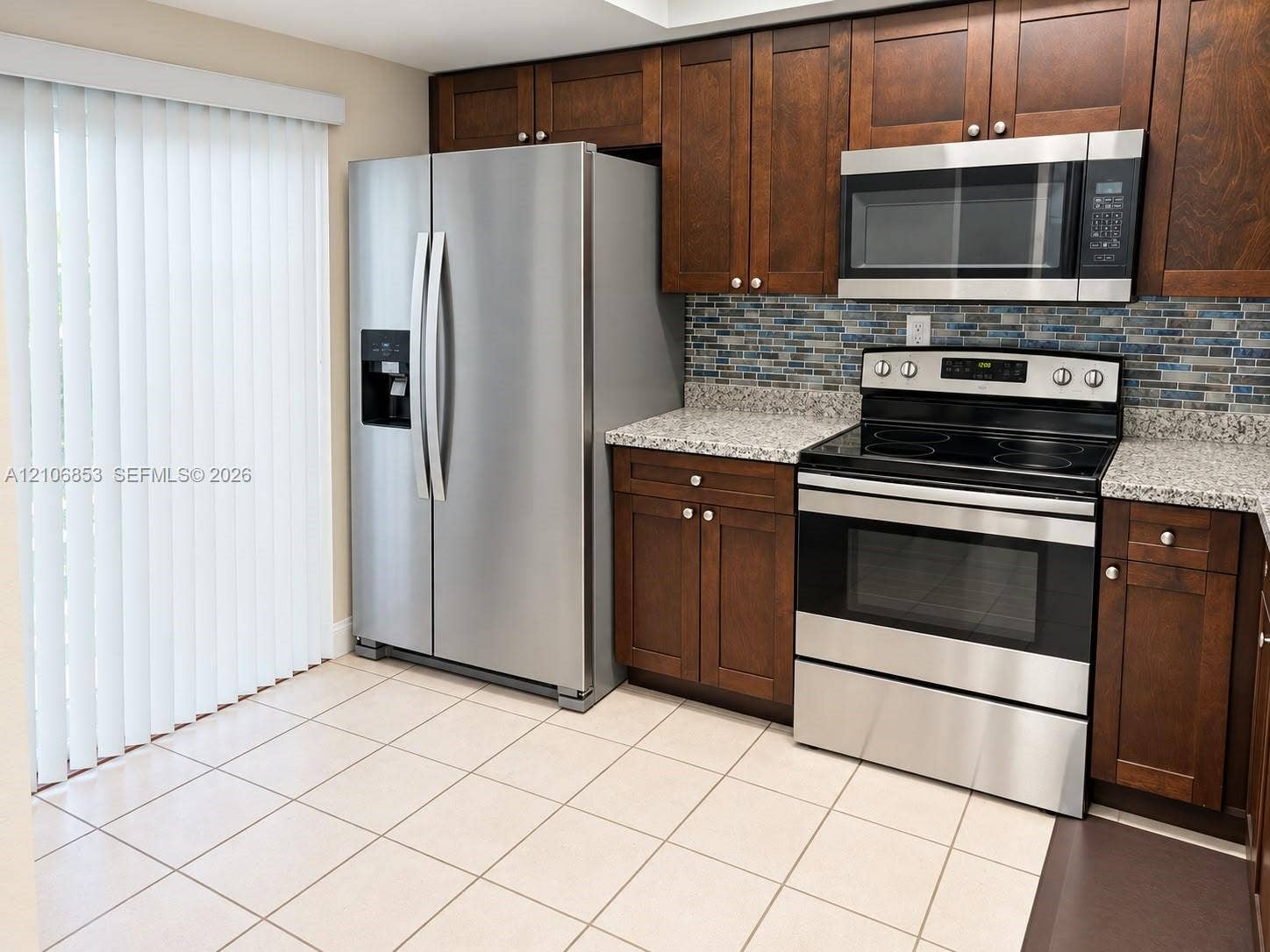 6331 Pinehurst Circle W, #C35, Tamarac, FL 33321 Kitchen featuring dark wood-finish cabinetry, stainless steel appliances, stone-look countertops, glass mosaic tile backsplash, and ceramic tile flooring