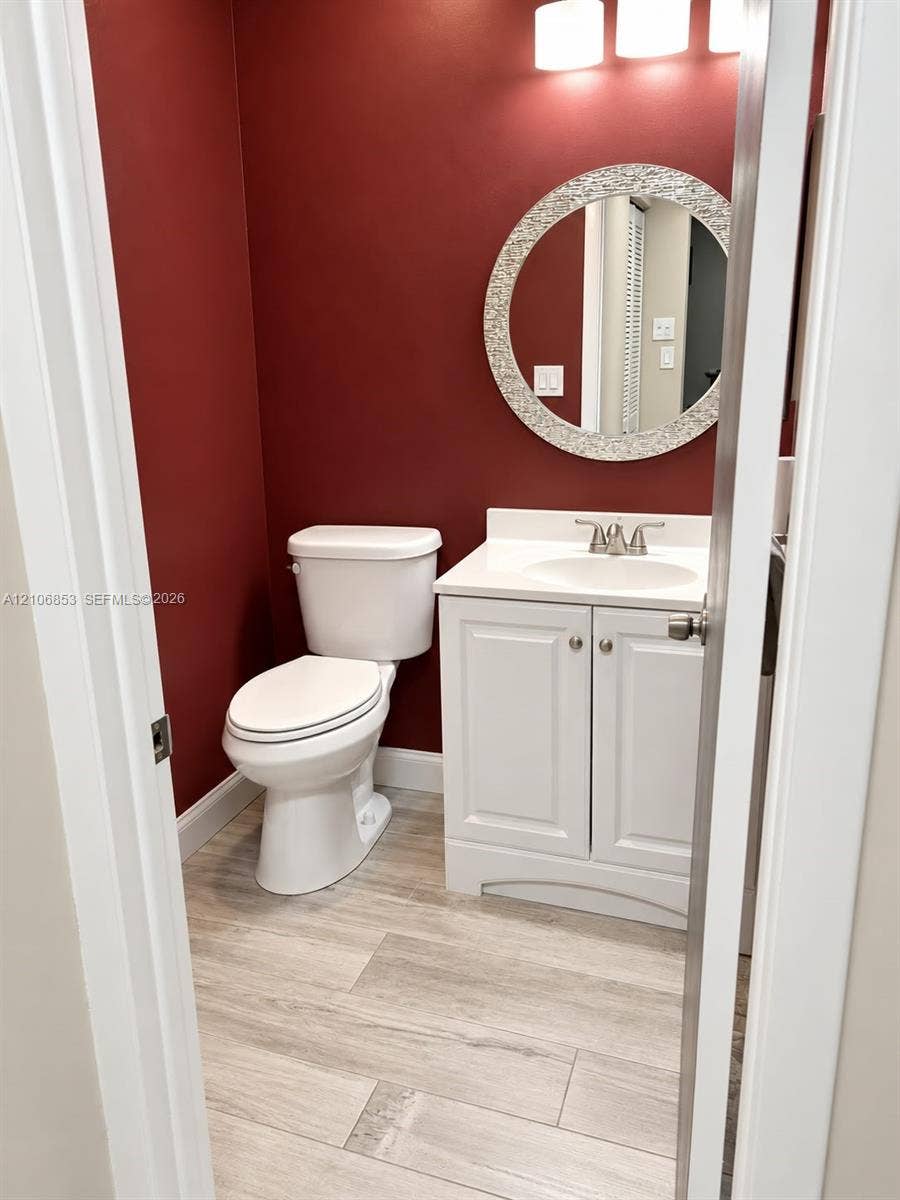 6331 Pinehurst Circle W, #C35, Tamarac, FL 33321 Bathroom featuring a white vanity cabinet with a solid surface countertop, an undermount sink, a circular mosaic-tile framed mirror, and wood-finish tile flooring