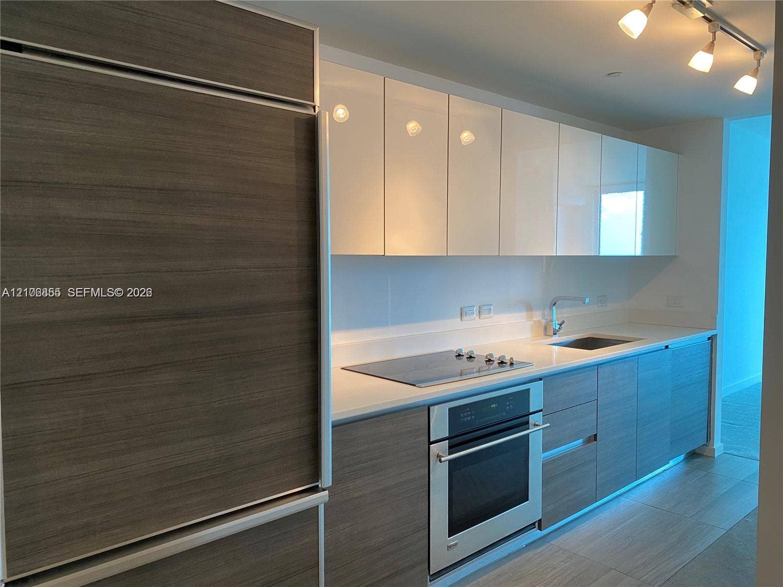 Kitchen featuring high-gloss upper cabinetry, wood-finish lower cabinetry, integrated refrigerator, solid-surface countertops, and stainless steel built-in oven