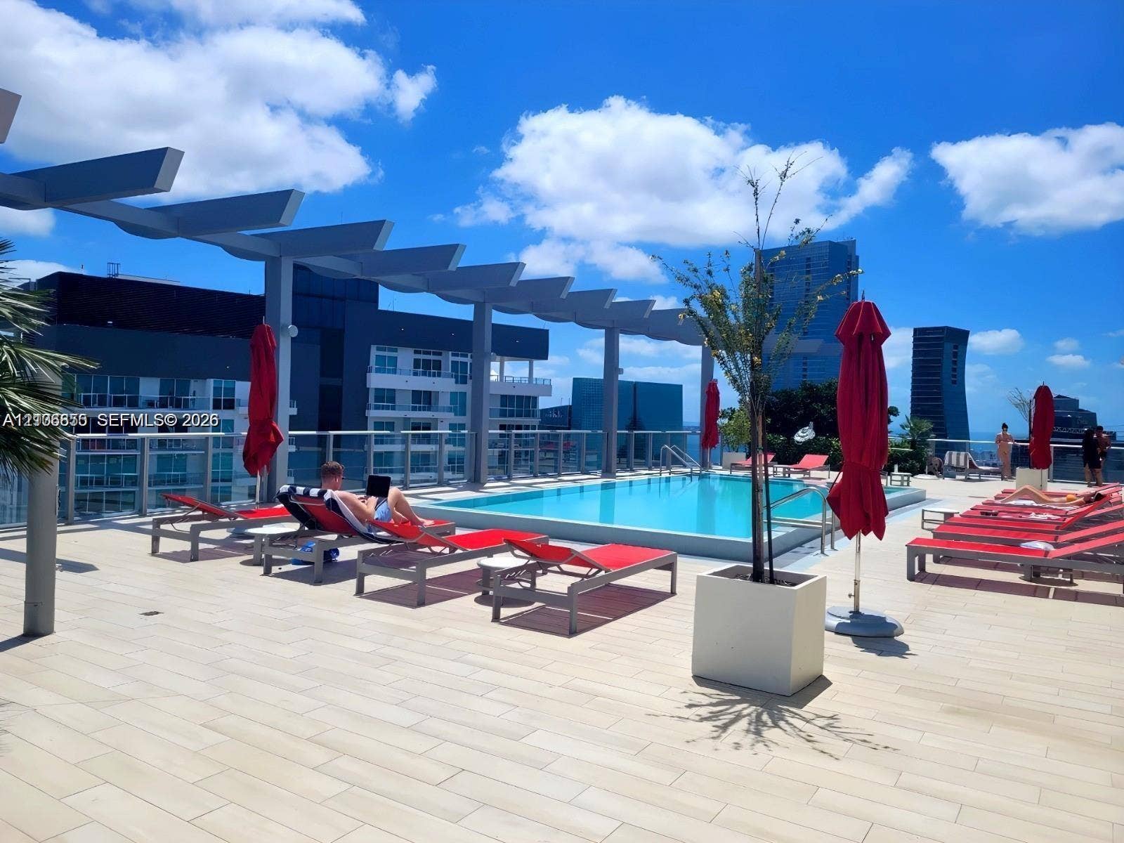 Rooftop pool deck featuring a geometric pergola, light-toned tiled flooring, and a glass panel railing
