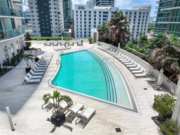 Swimming pool featuring a sun shelf, integrated steps, light-colored tile decking, and landscaping