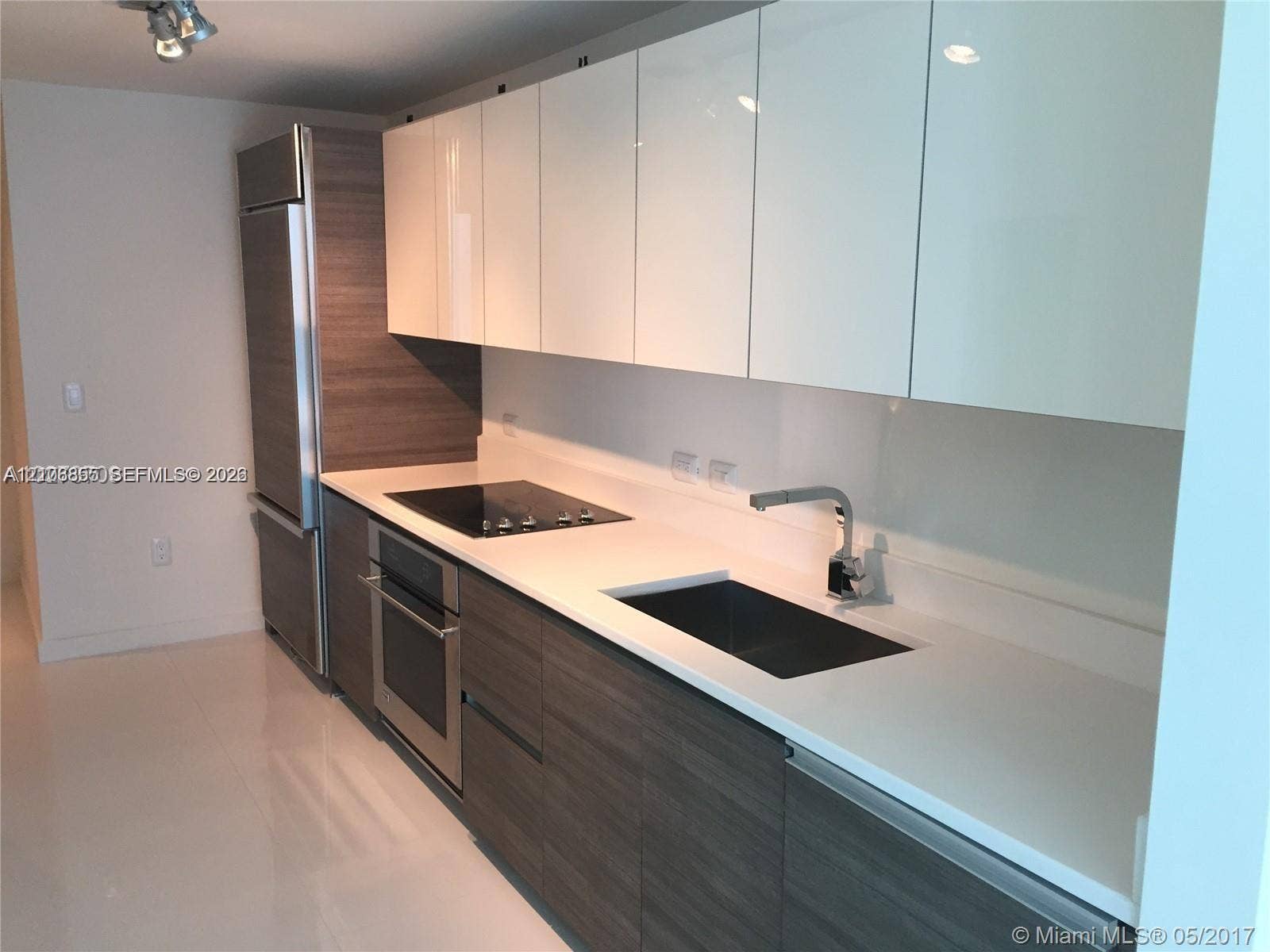 Contemporary kitchen featuring gloss-finish upper cabinetry, wood-finish lower cabinetry, integrated stainless steel appliances, solid-surface countertops, and an undermount sink with a modern gooseneck faucet