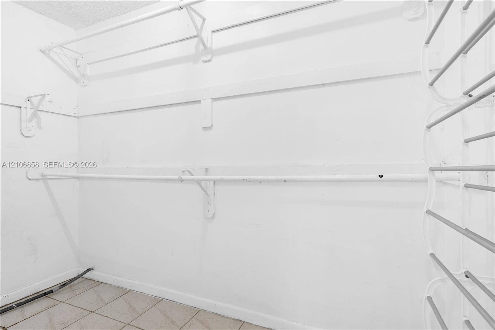 10960 SW 25th Street, Miami, FL 33165 Storage area featuring white built-in shelving, metal garment rods, and ceramic tile flooring