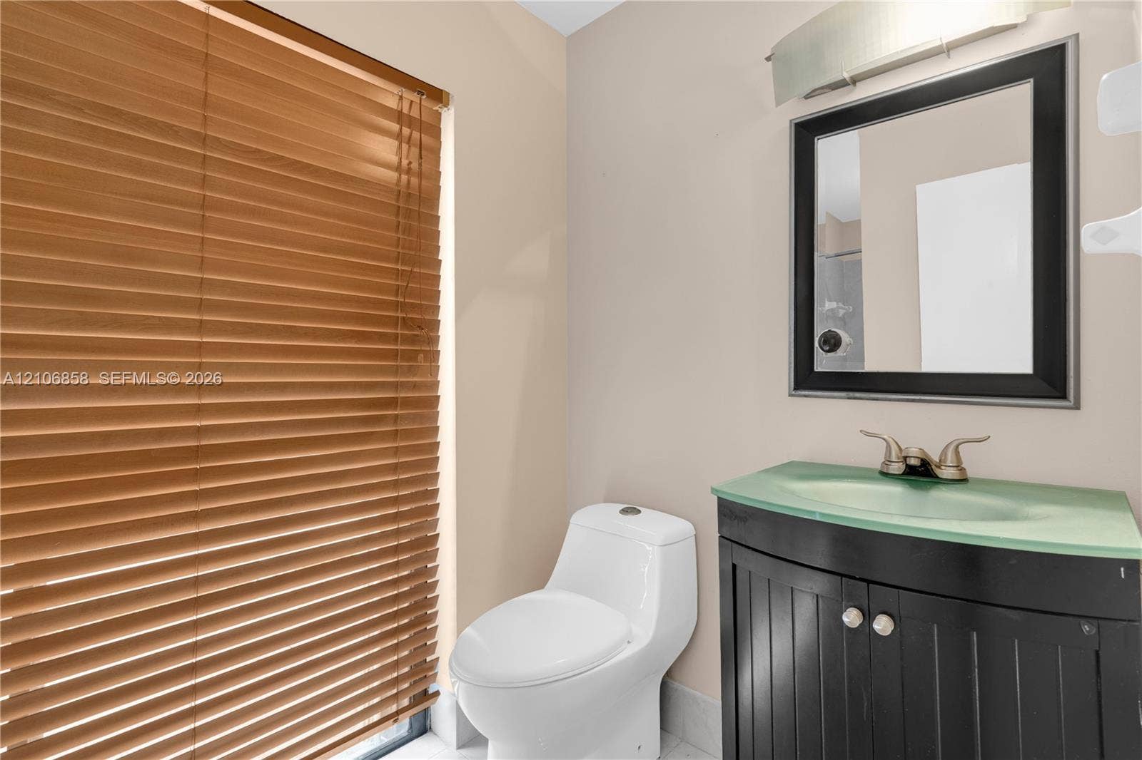 10960 SW 25th Street, Miami, FL 33165 Vanity cabinet with a molded integrated sink and countertop, framed wall mirror, polished metallic fixtures, and wood-finish window blinds