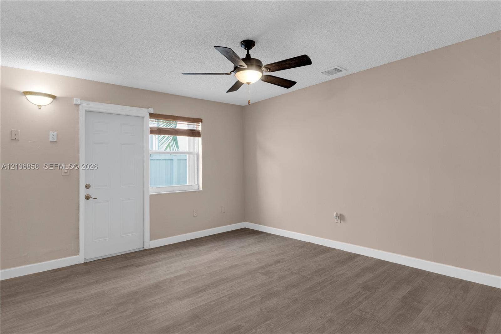 10960 SW 25th Street, Miami, FL 33165 Neutral-toned interior room featuring wood-finish flooring, a ceiling fan with integrated lighting, a single exterior door, and a wall-mounted sconce