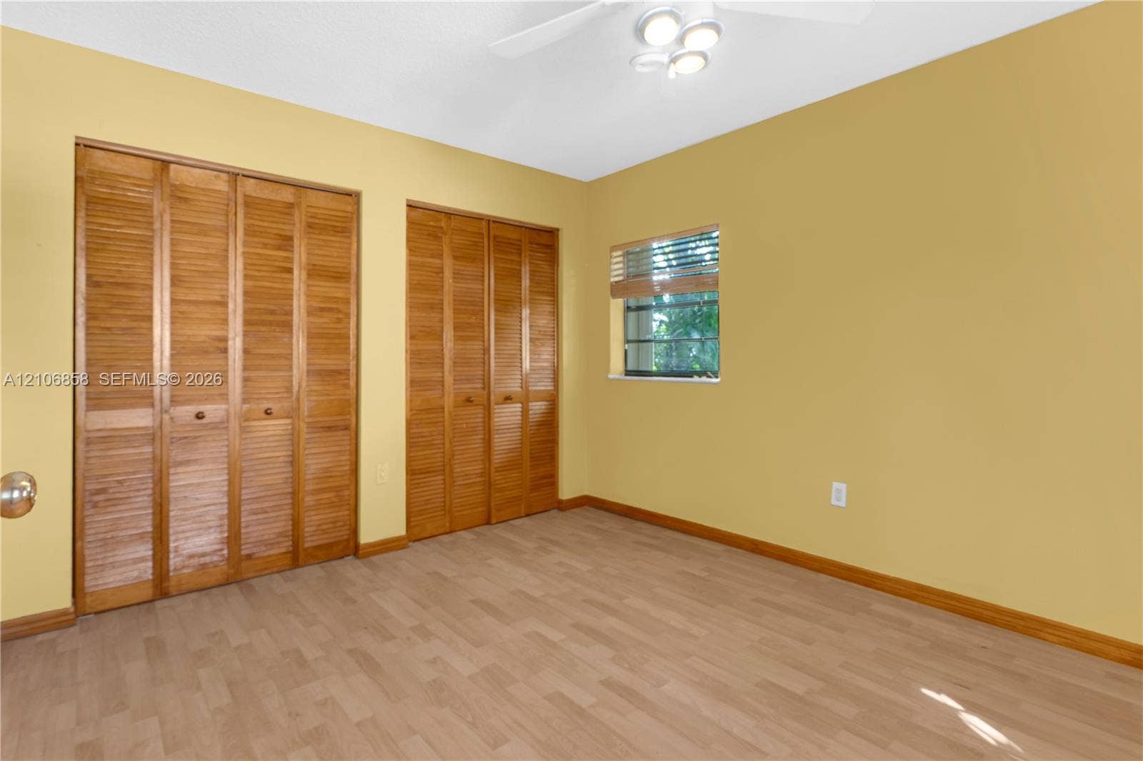 10960 SW 25th Street, Miami, FL 33165 Wood-finish flooring, two sets of bifold wooden closet doors, and a ceiling-mounted light fixture
