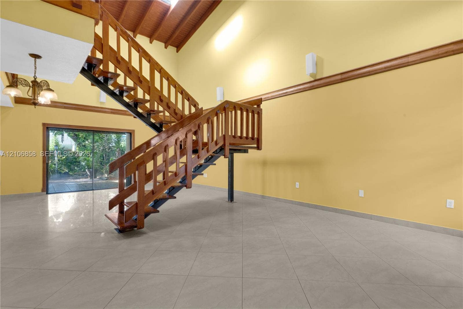 10960 SW 25th Street, Miami, FL 33165 Vaulted ceiling with exposed wood-beam detailing, open-tread staircase with wood railings, large-format tile flooring, and oversized sliding glass doors