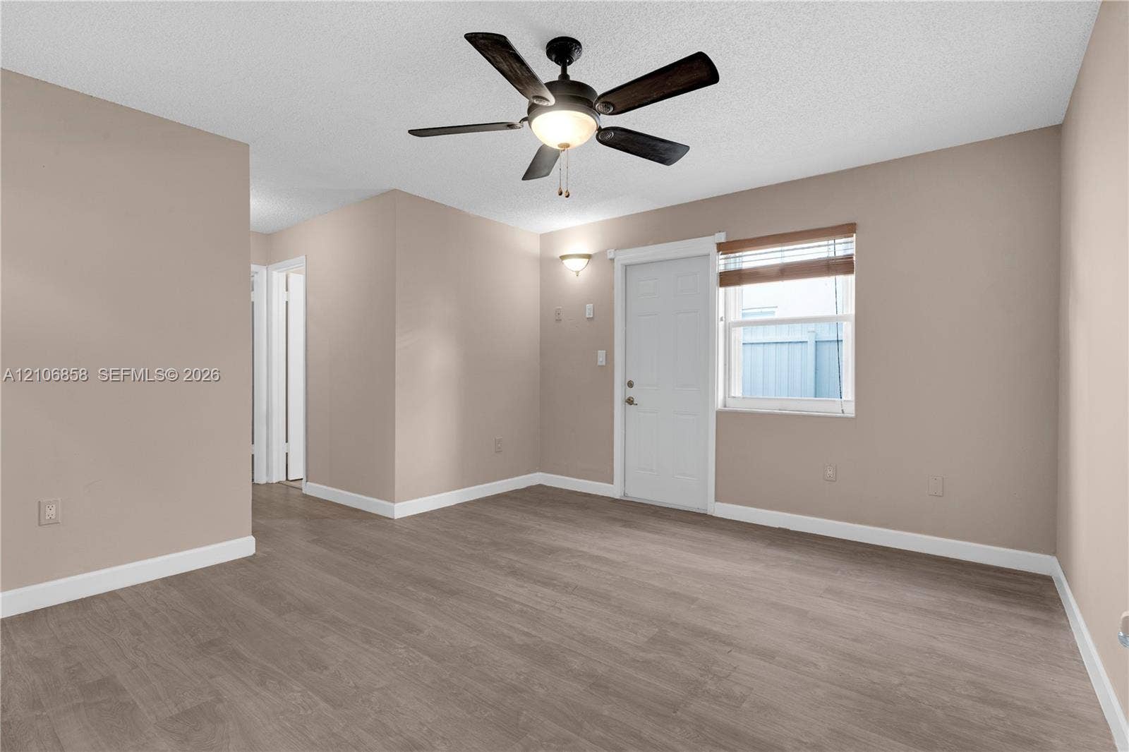 10960 SW 25th Street, Miami, FL 33165 Neutral-toned room featuring wood-finish flooring, a central ceiling fan with integrated lighting, wall-mounted accent lighting, and a single-panel door