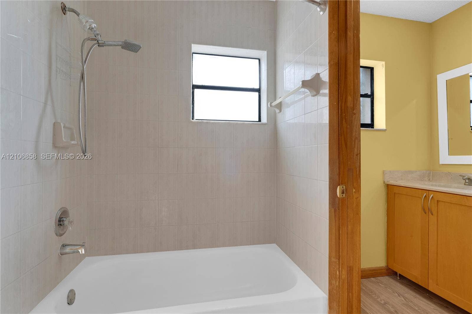 10960 SW 25th Street, Miami, FL 33165 Bathroom featuring a tub-shower combination with light-toned ceramic tile surround, a hand-held showerhead, and a vanity cabinet with a solid surface countertop