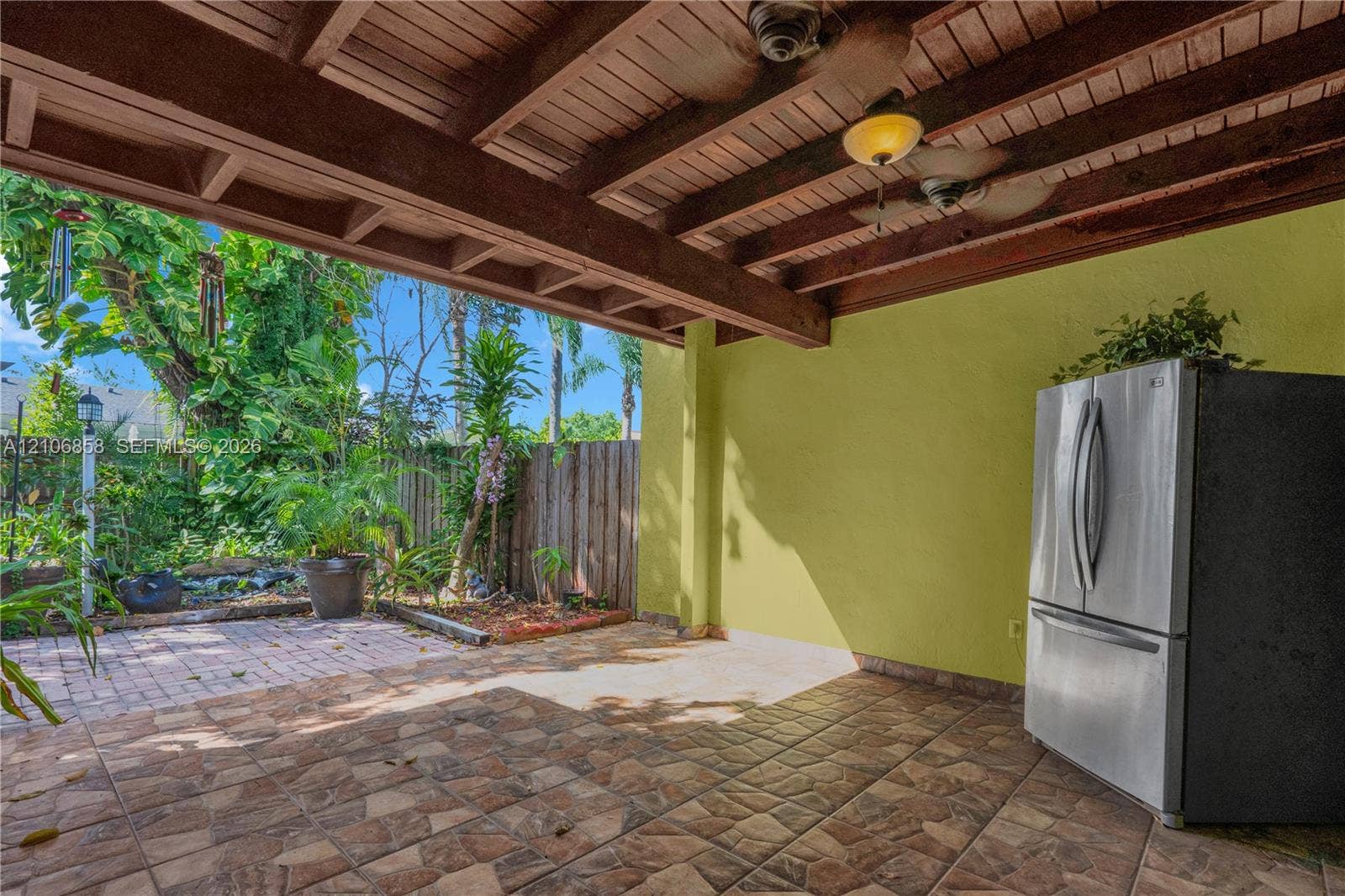 10960 SW 25th Street, Miami, FL 33165 Covered patio featuring an exposed wood-beam ceiling with mounted ceiling fans, tiled flooring, built-in stainless steel refrigerator, and hardscaped brick detailing