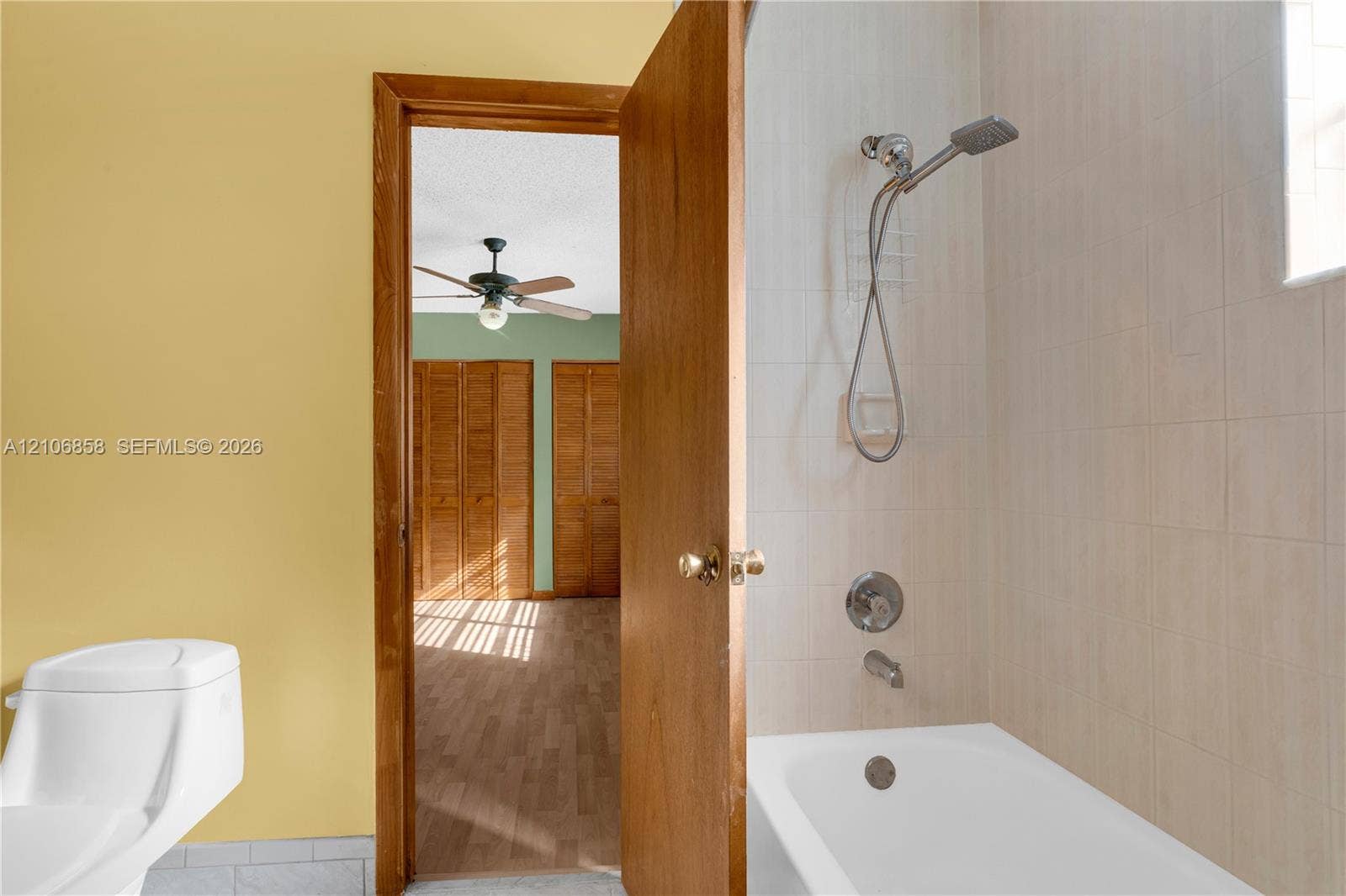 10960 SW 25th Street, Miami, FL 33165 Bathroom featuring a white bathtub with a handheld shower fixture and tiled surround, accompanied by a white toilet