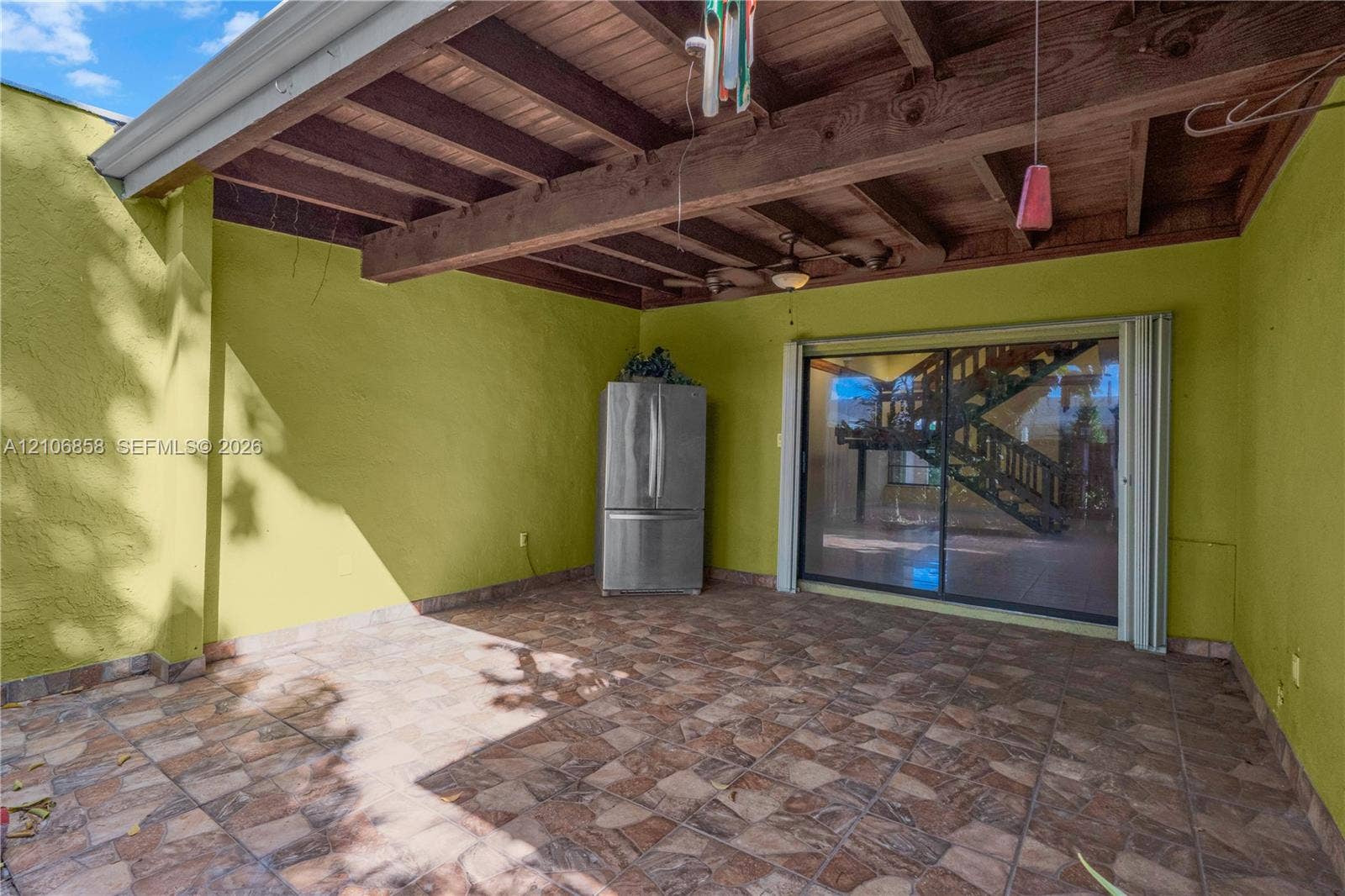 10960 SW 25th Street, Miami, FL 33165 Covered patio featuring an exposed wood-beam ceiling, stone-tile flooring, ceiling fan, and sliding glass door