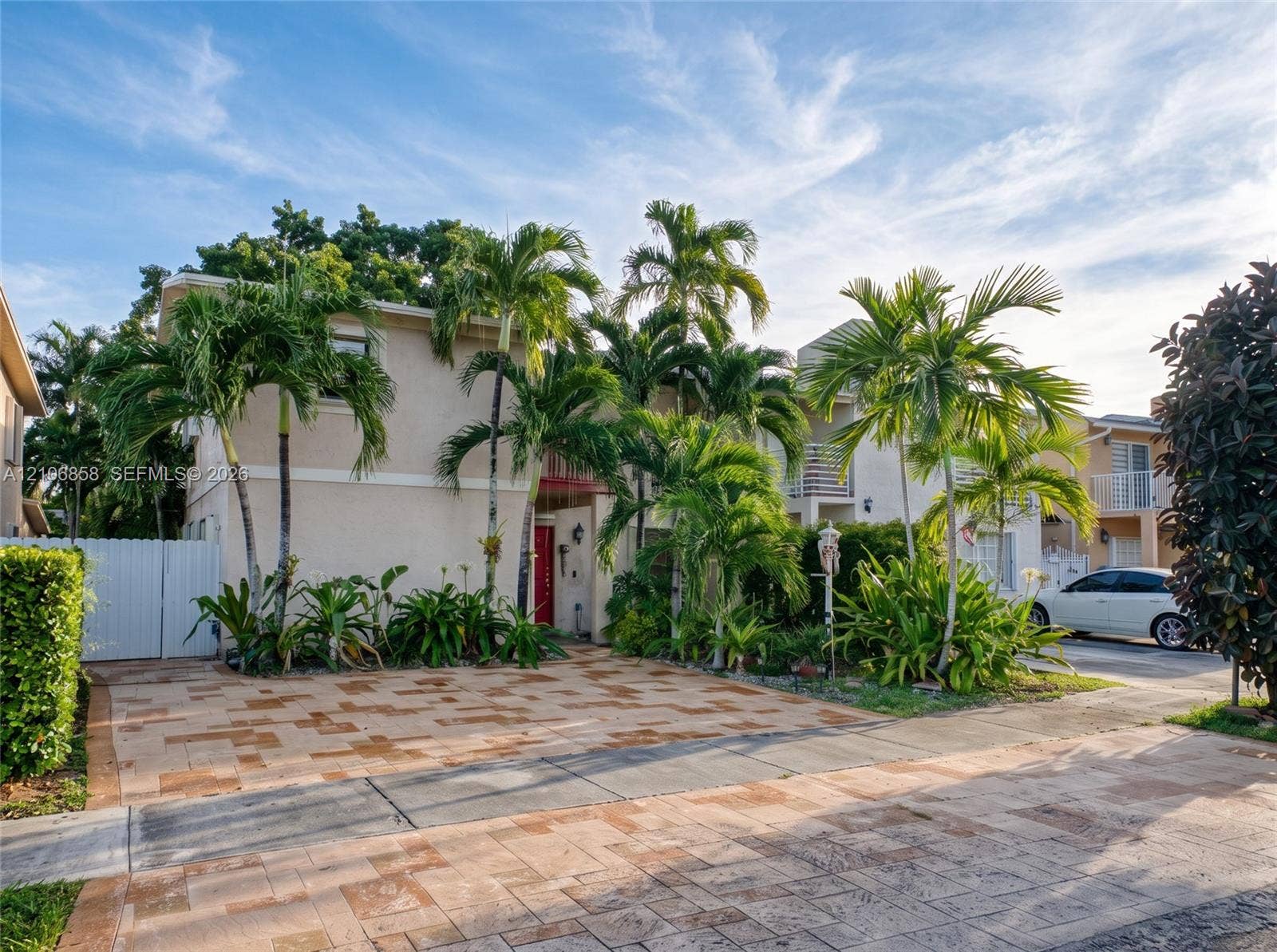 10960 SW 25th Street, Miami, FL 33165 Multi-level exterior featuring a smooth stucco finish, paved driveway, second-story balcony, and established palm trees