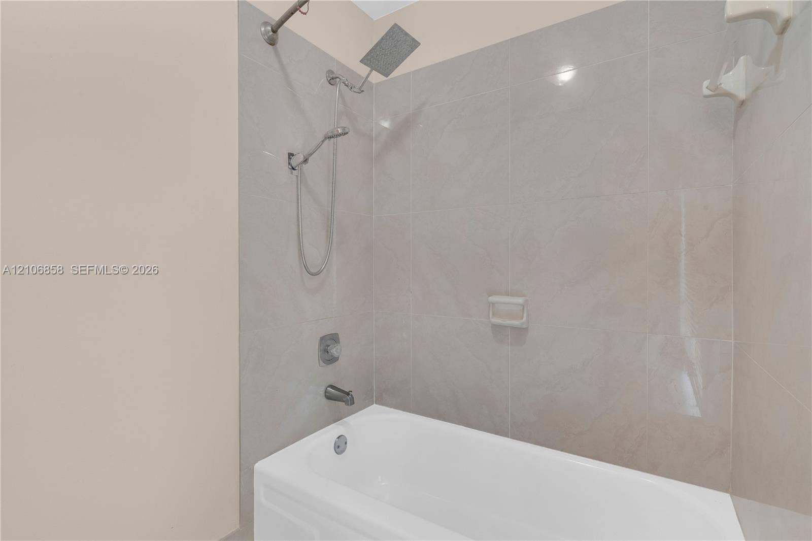10960 SW 25th Street, Miami, FL 33165 Bathtub surround with neutral-toned oversized wall tile, rainfall shower head, handheld shower fixture, and integrated soap niche