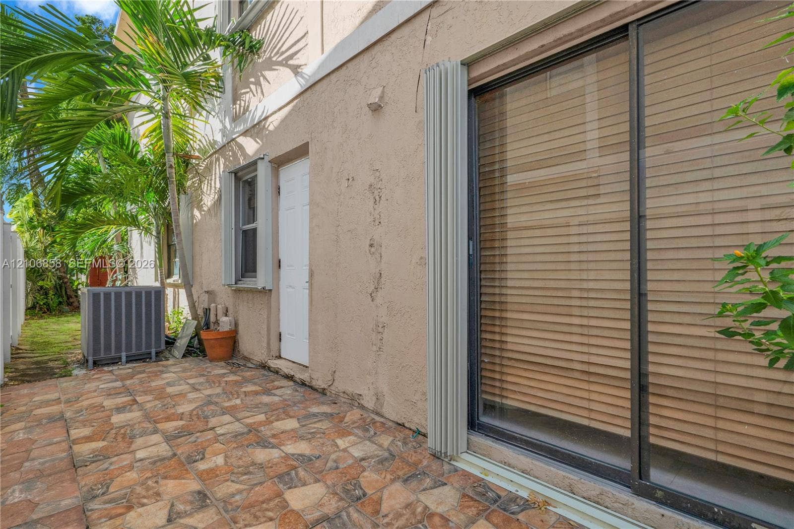 10960 SW 25th Street, Miami, FL 33165 Exterior patio featuring multi-toned tile flooring, stucco wall finish, sliding glass doors, and a pedestrian door