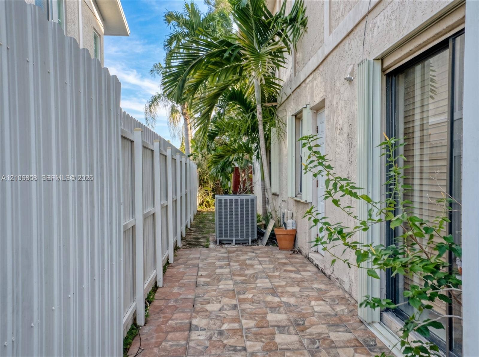 10960 SW 25th Street, Miami, FL 33165 Side exterior featuring a paved stone-patterned walkway, white corrugated metal fencing, and stucco siding
