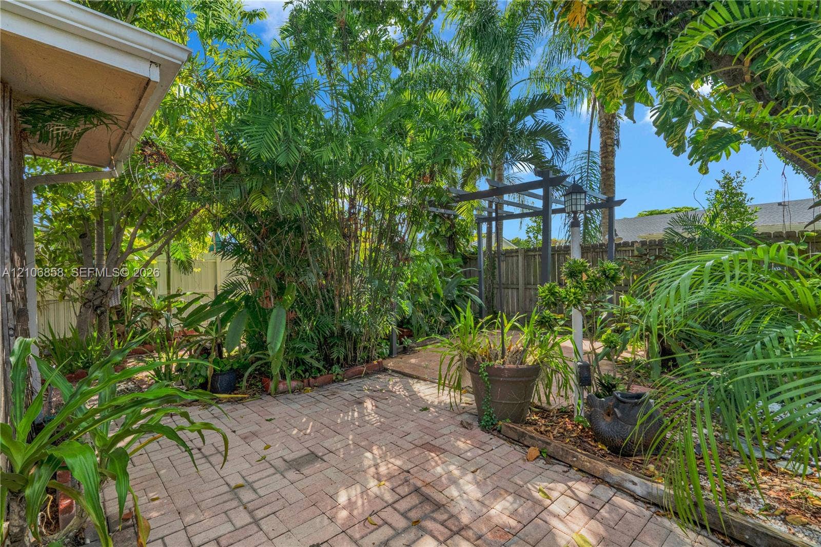 10960 SW 25th Street, Miami, FL 33165 Brick paver patio featuring a wooden pergola, privacy fencing, and lush tropical landscaping