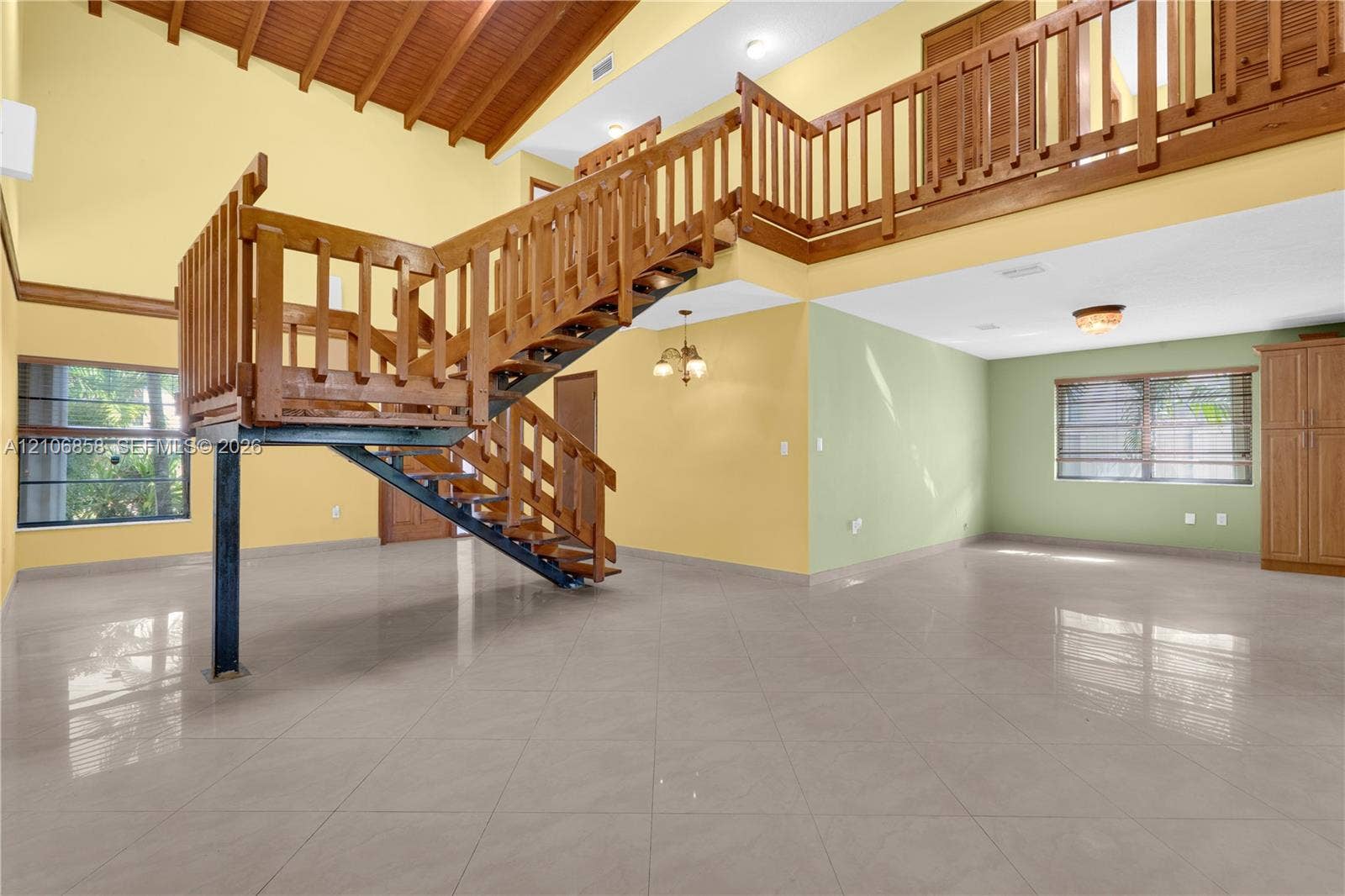 10960 SW 25th Street, Miami, FL 33165 Vaulted wood-plank ceiling, structural metal staircase with wood railing, mezzanine balcony, large-format tile flooring, and built-in cabinetry