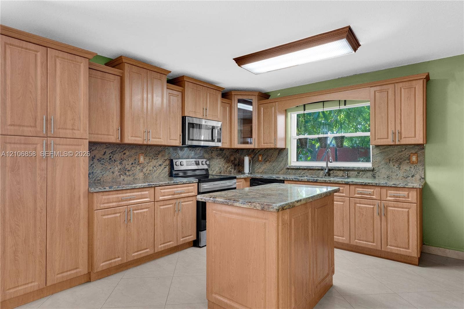 10960 SW 25th Street, Miami, FL 33165 Kitchen featuring wood-finish cabinetry, natural stone countertops, a center island, stainless steel microwave, and tile flooring