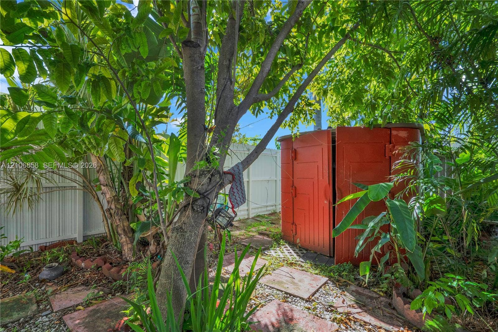 10960 SW 25th Street, Miami, FL 33165 Private backyard featuring mature landscaping, a circular storage structure, stone paver pathway, and solid perimeter fencing