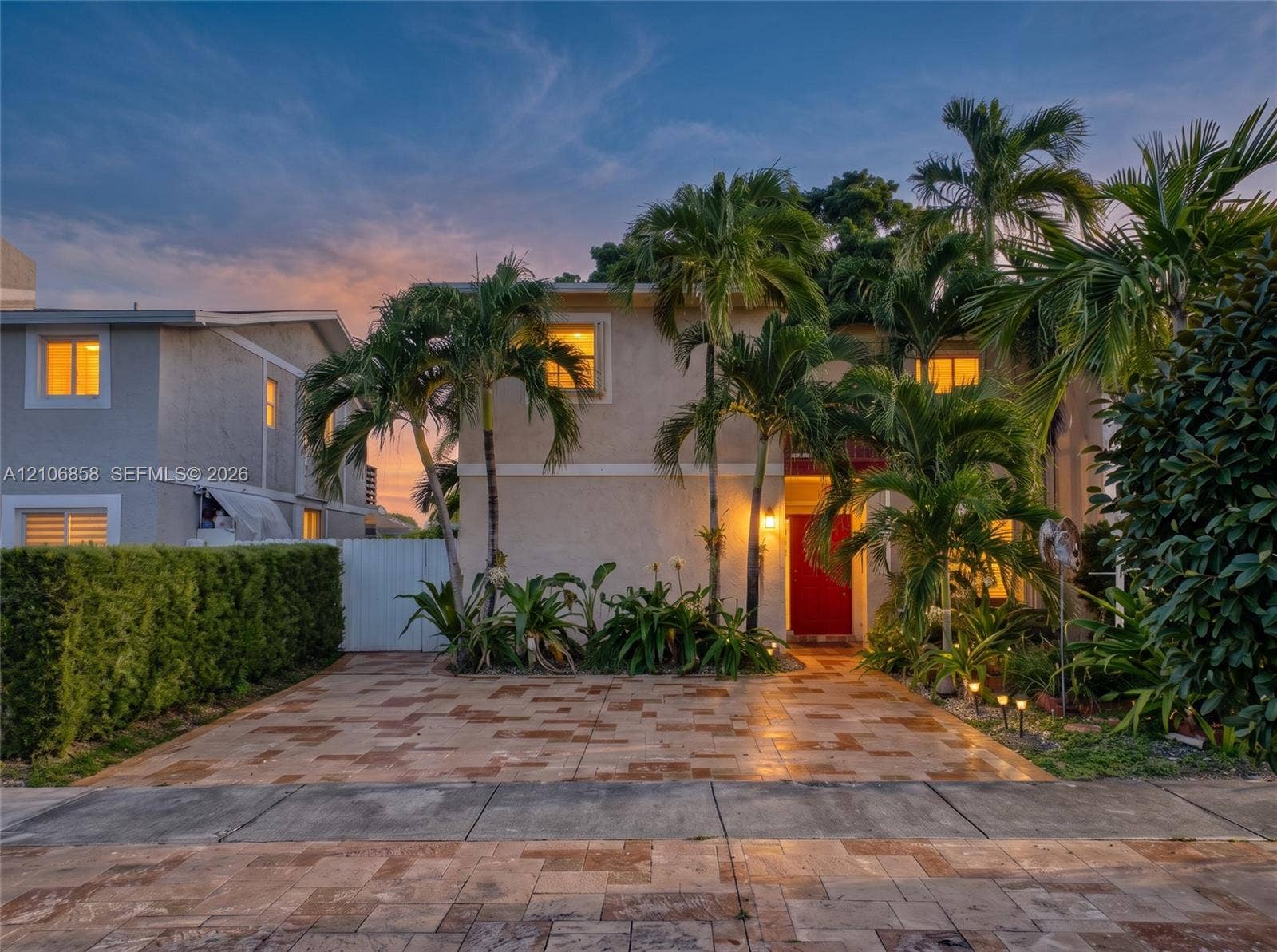 10960 SW 25th Street, Miami, FL 33165 Two-story stucco exterior featuring a paved stone driveway, mature palm trees, manicured hedges, and a vibrant red front door