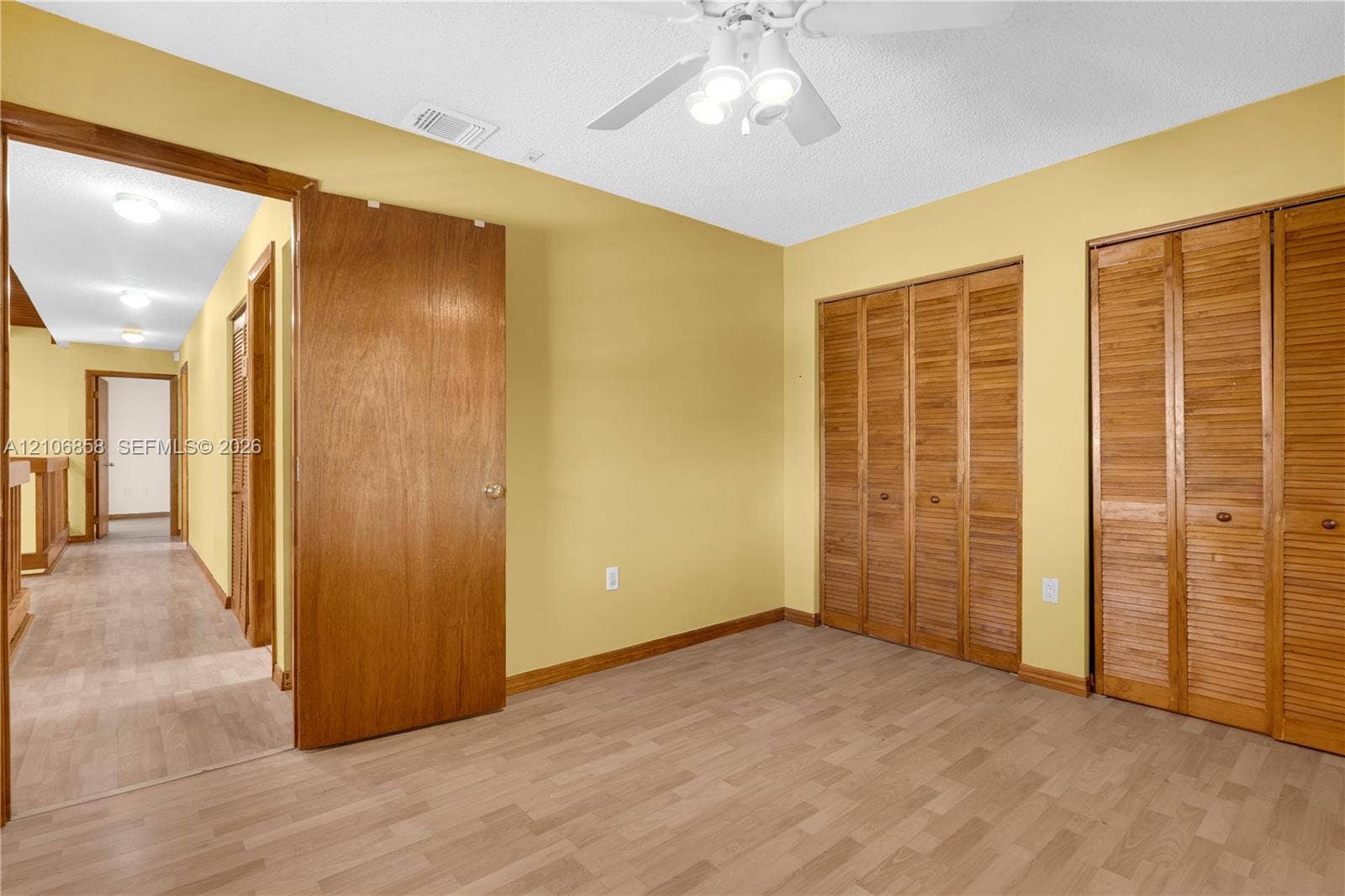 10960 SW 25th Street, Miami, FL 33165 Wood-finish flooring, dual bi-fold wooden closet doors, and a ceiling-mounted light fixture with a fan